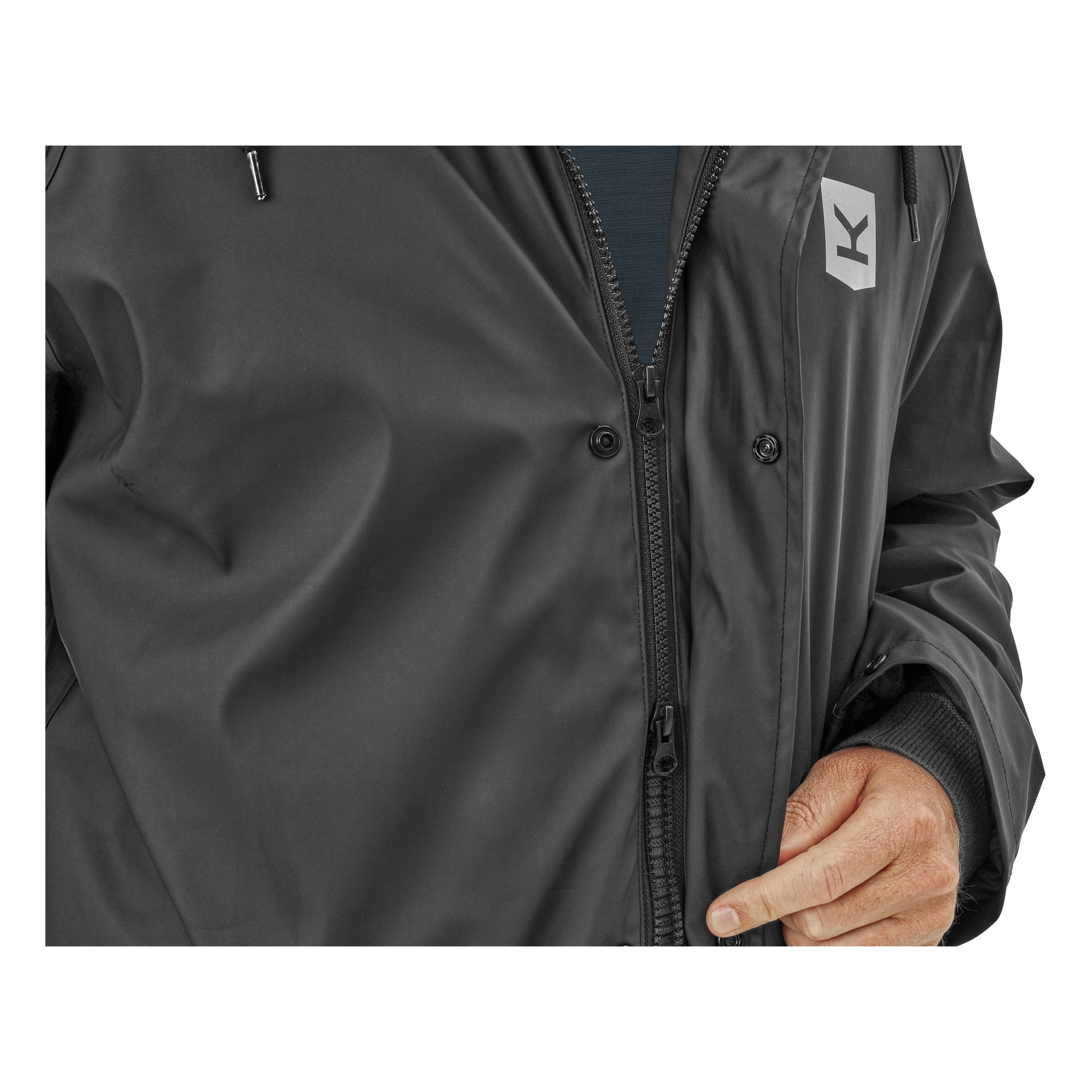 Die Hand einer Person wird gezeigt, wie sie den Reißverschluss einer schwarzen, fleecegefütterten Visby-Regenjacke von Kayoba Outdoor Männern mit einem kleinen Brustlogo verstellt. Nur die Hand und ein Teil des Oberkörpers sind sichtbar.