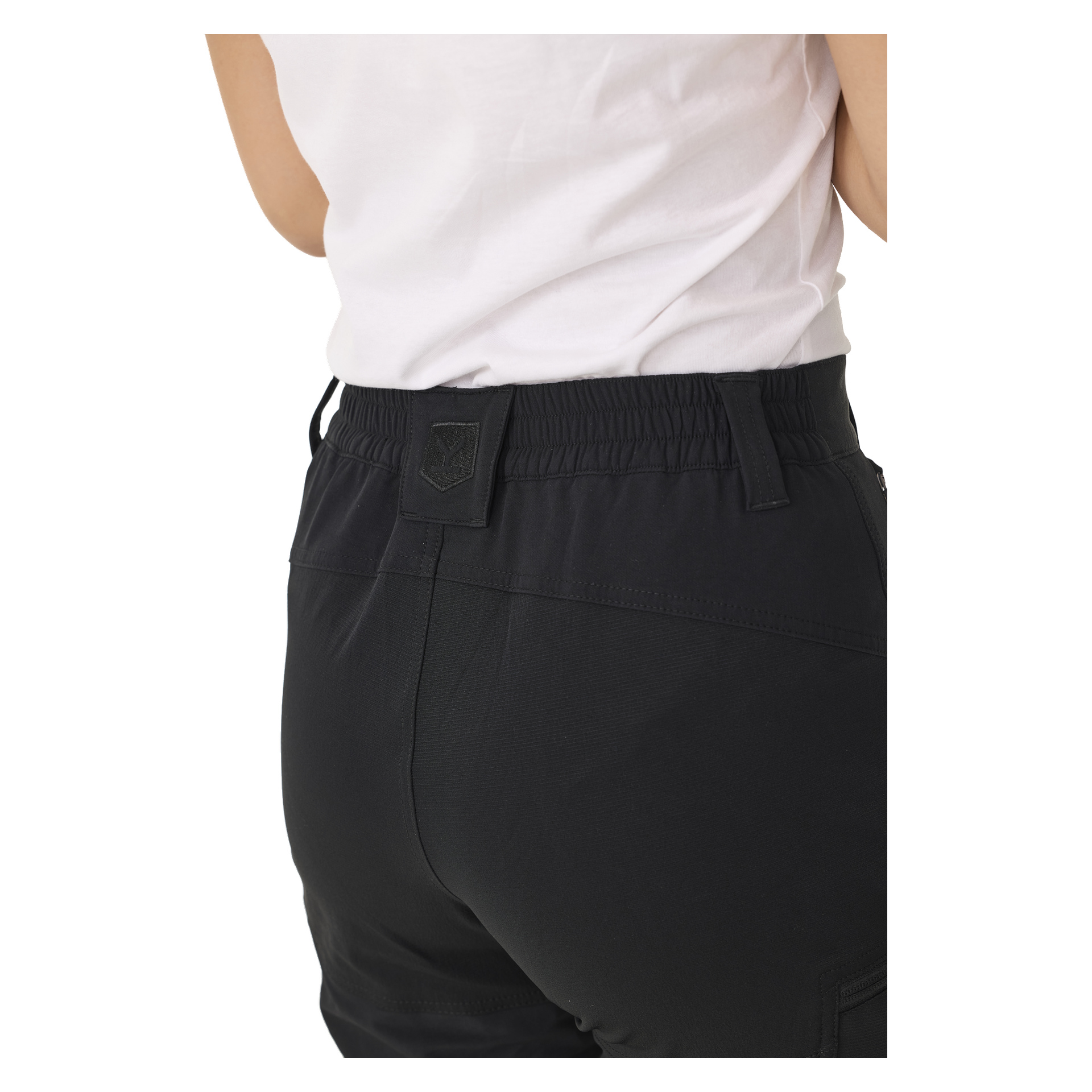 En bakifrån vy av en person klädd i en vit T-shirt och svarta Kayoba Outdoor Women's Abisko-byxor med dragkedjeben. Byxorna har ett elastiskt midjeband och en liten rektangulär lapp nära bältesöglan. Bilden visar endast personen från midjan och ner till ovanför knäna.
