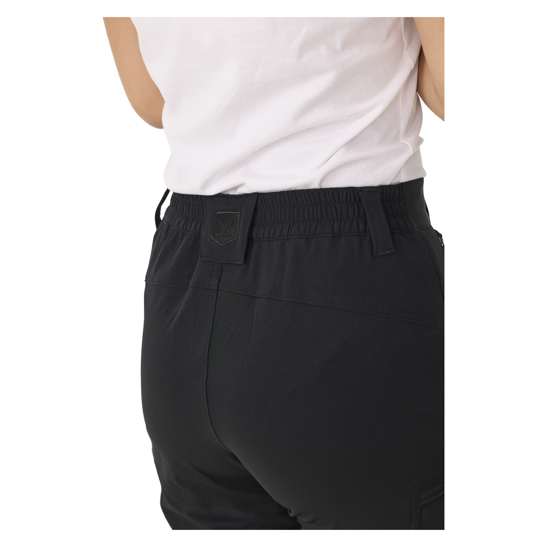 En person avbildas från midjan och nedåt och ses bakifrån, klädd i en vit skjorta och svarta Kayoba Outdoor Women's byxor med dragkedje, med resår i midjan och en svart lapp på ryggen.
