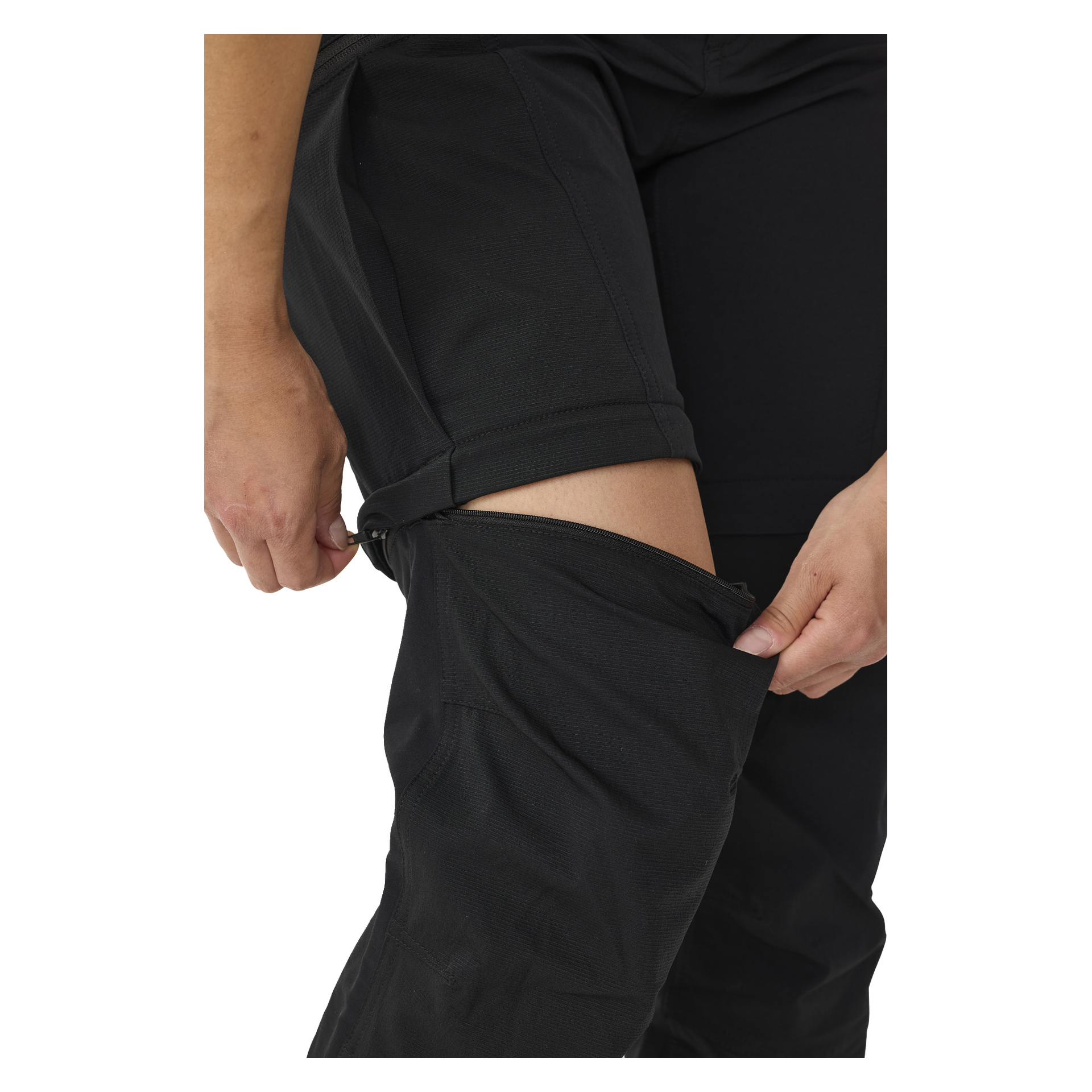 En person drar ner dragkedjan på underbensdelen av Kayoba Outdoor Women's utomhusbyxor med zip-off benen Abisko, vilket visar knä och överben. Fokus ligger på händerna och byxorna.