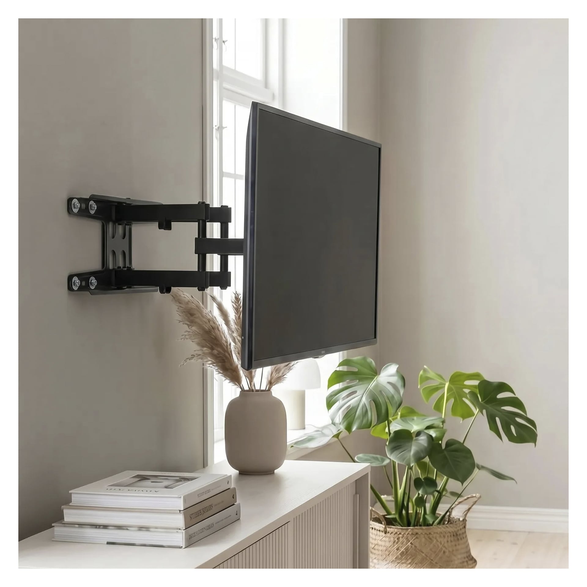 En platt-TV är monterad på väggen med Bright Wall-fästet bredvid ett fönster. Under det visar ett beige skåp en vas med torkat gräs och en liten hög böcker, medan en bladgrön växt står på golvet till höger.