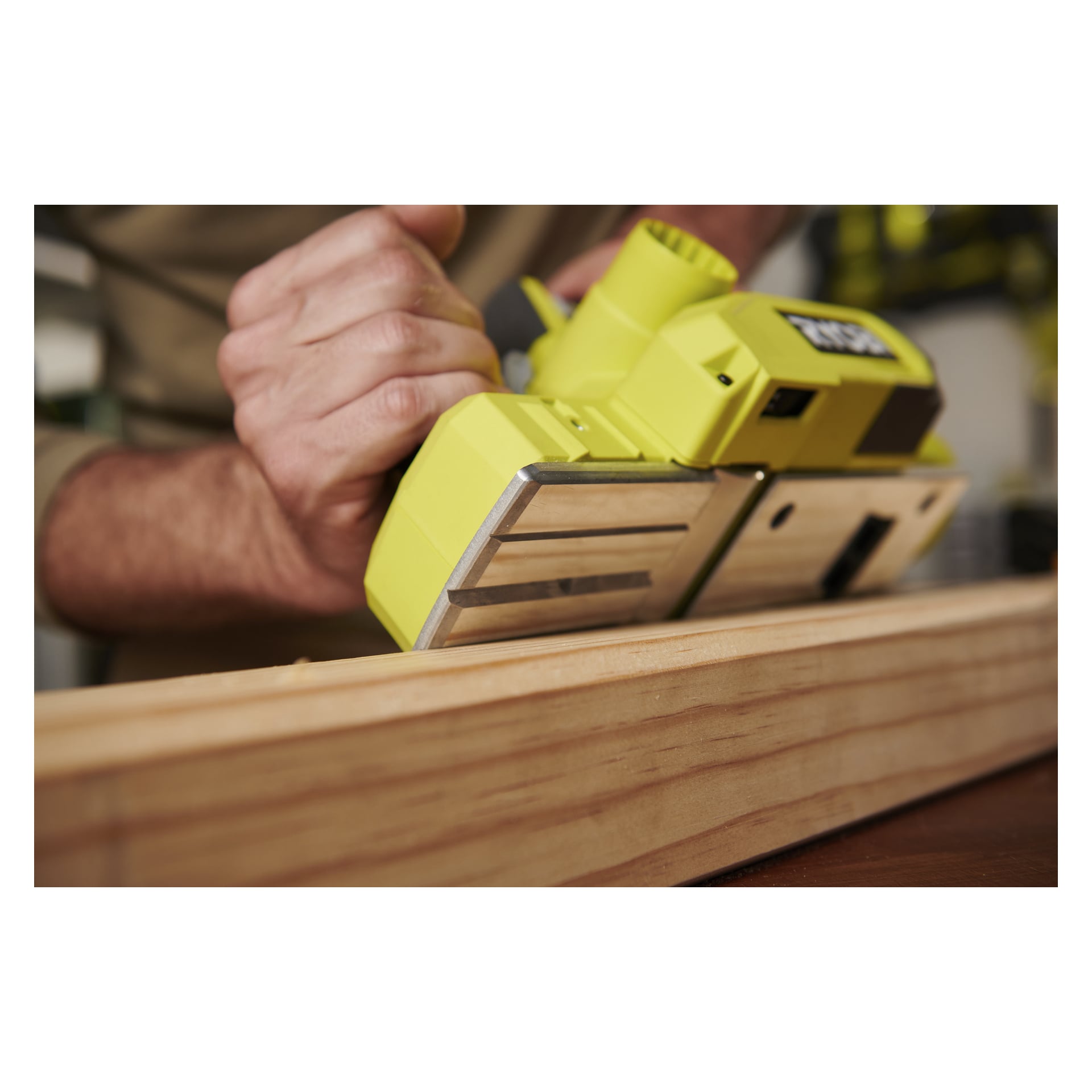 Ktoś obsługuje Ryobi One+ Cordless Electric Planer RPL18-0 na drewnianej desce, mocno przyciskając narzędzie do drewna. Nacisk kładzie się na wygładzenie zarówno struga, jak i deski.