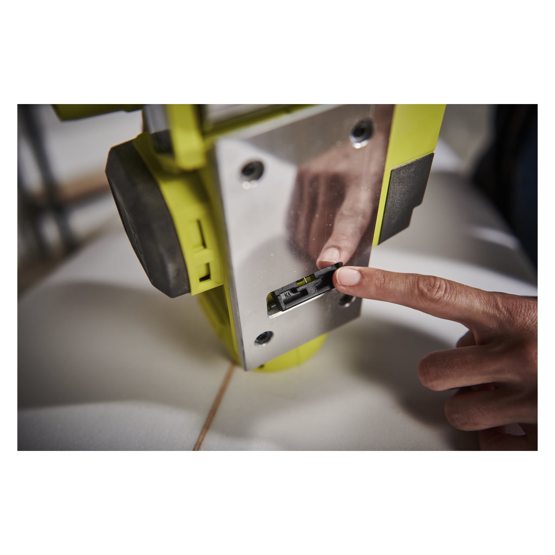 Palec osoby reguluje przesuwany przełącznik w żółto-srebrnym Ryobi One+ Cordless Electric Planer RPL18-0, z drewnianą powierzchnią poniżej.