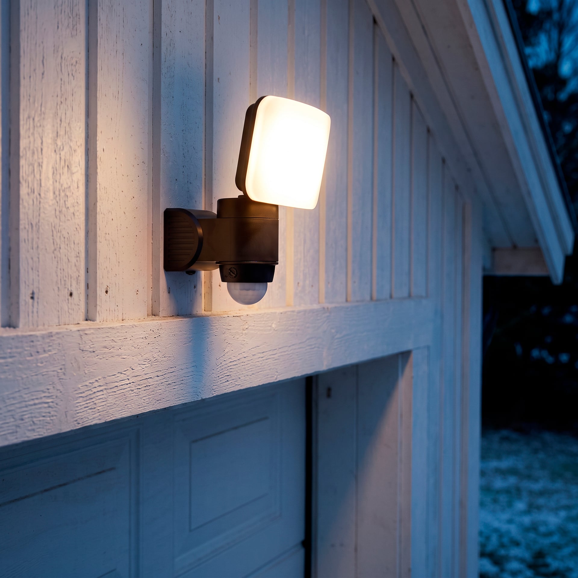 Eine Anslut-Bewegungssensor-LED-Lampe, die auf einem Holzgebäude montiert ist und ein warmes Licht ausstrahlt.