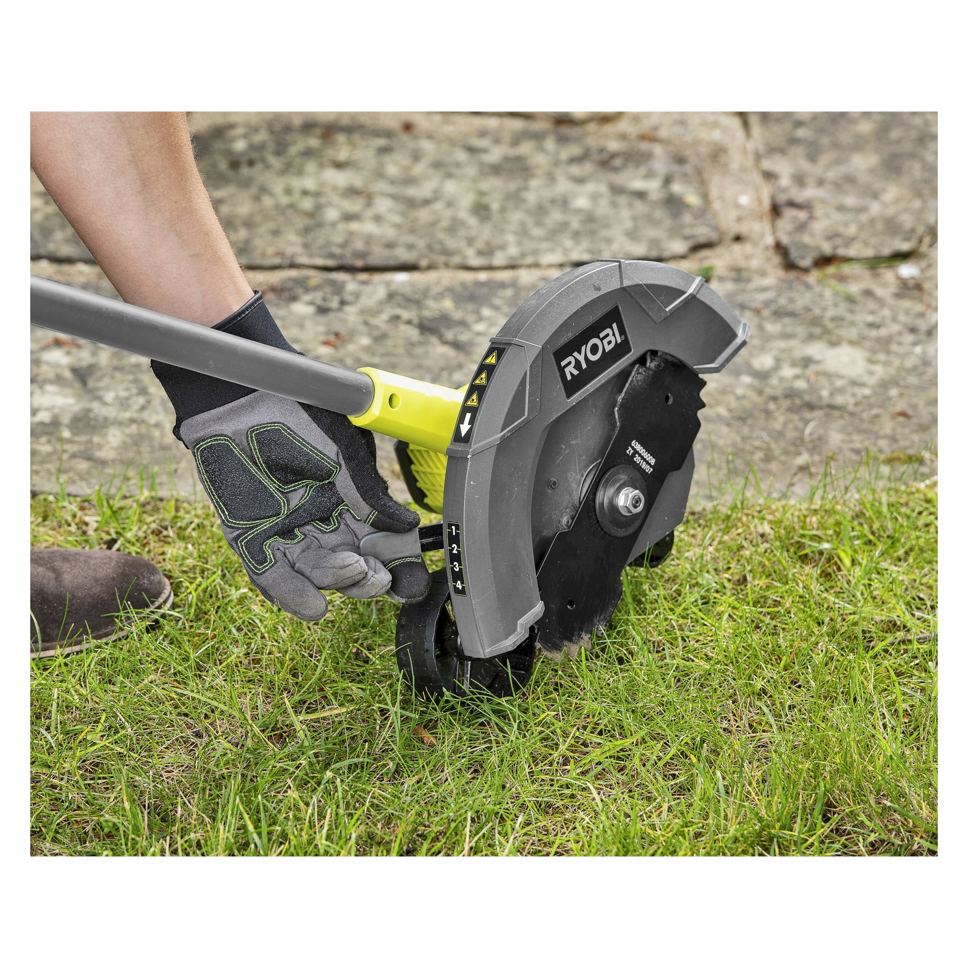 Noen med hanske bruker en Ryobi One+ Edge-trimmer RY18EGA-0 for å rydde kanten av en gresskledd plen nær en steinsti.