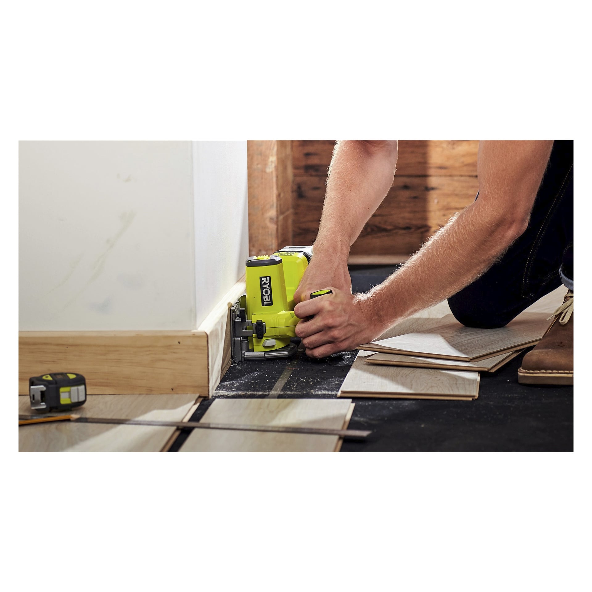 Knäböjande vid en vägg använder man en Ryobi One+ Multi-saw R18MMS-0 för att skära laminatgolv, med flera golvbrädor och ett måttband i närheten.