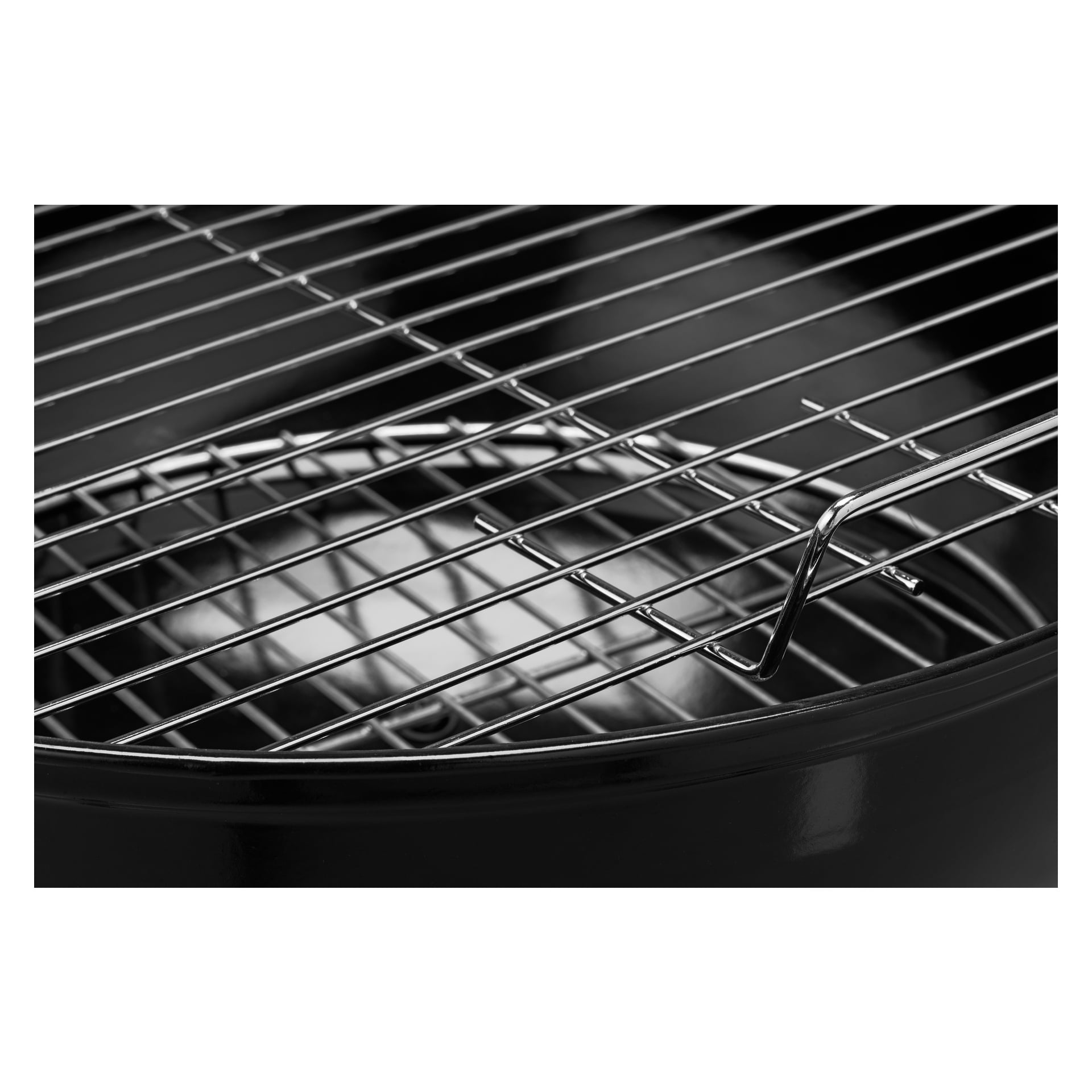 Szczegółowe spojrzenie na lśniącą, nieskazitelną metalową kratkę kraty spoczywającą na grillu Burns & Barkles Kettle Grill Coal King 430. Zdjęcie podkreśla wypolerowane pręty i górną krawędź okrągłego, czarnego grilla węglowego, bez jedzenia i sztućców.
