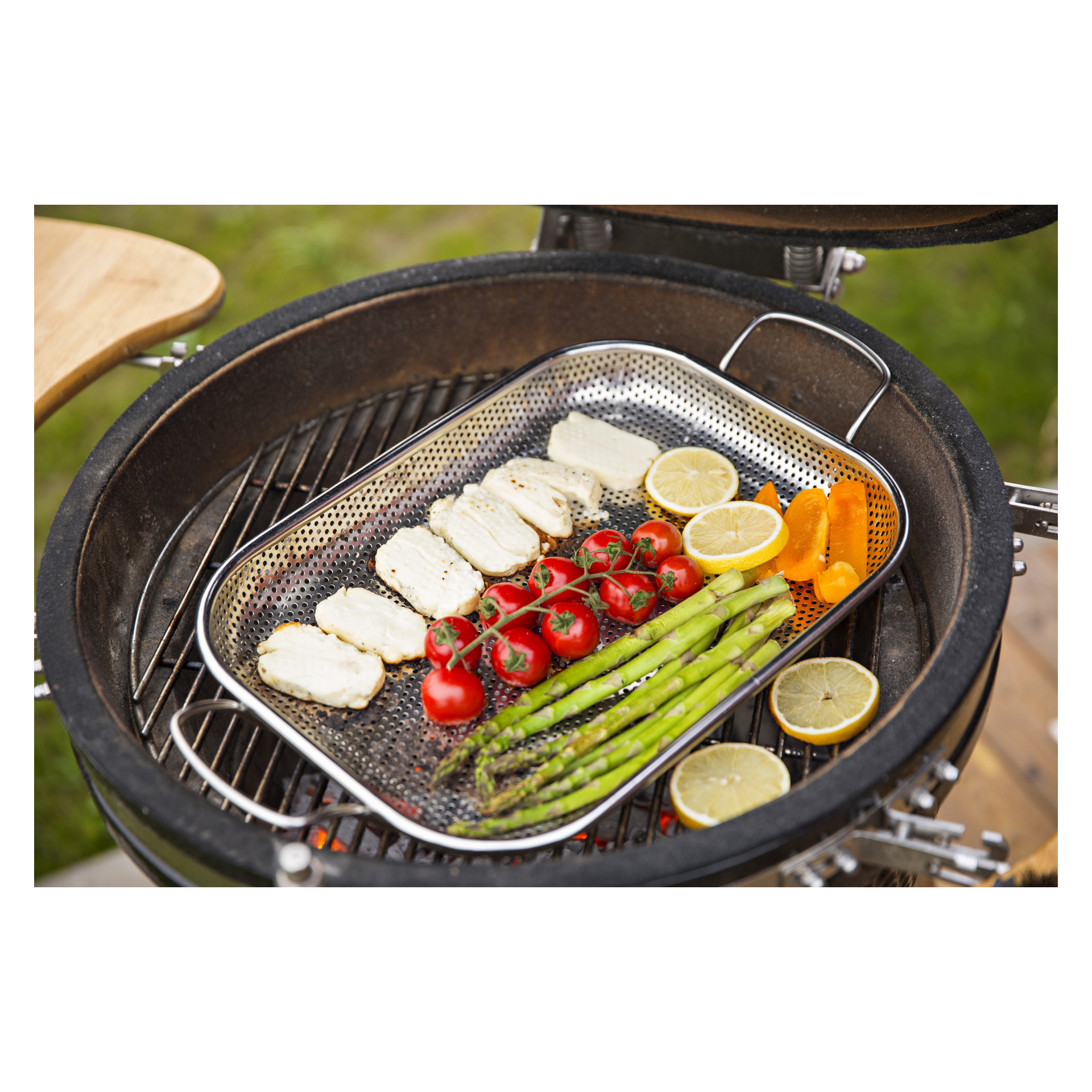 På en grill i trädgården innehåller en Burns & Barkles Grill-panna halloumi-ostskivor, körsbärstomater som fortfarande sitter kvar på rankan, sparrisspjut, remsor av orange paprika samt både halverade och skivade citroner.