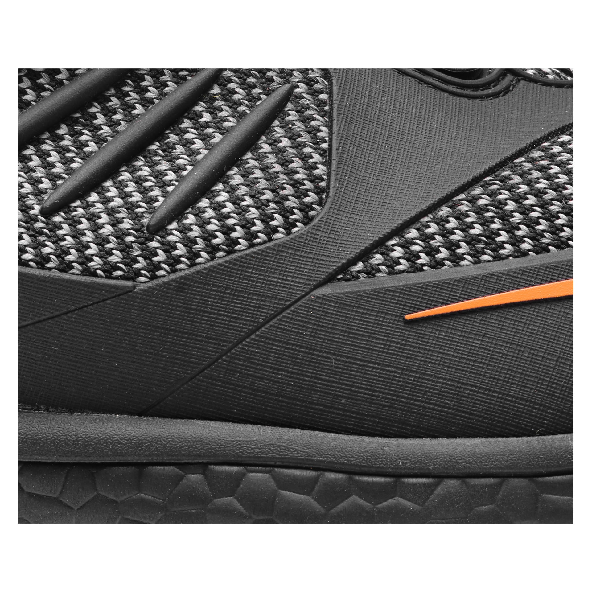 Detaljerad vy av Bluewear Pro Workwear Madison säkerhetsskor, som har en svart texturerad stickad överdel accentuerad av gummiränder och en orange linje. Sulan är mönstrad med hexagoner, och skon växlar mellan nätsektioner och syntetiska överlägg.