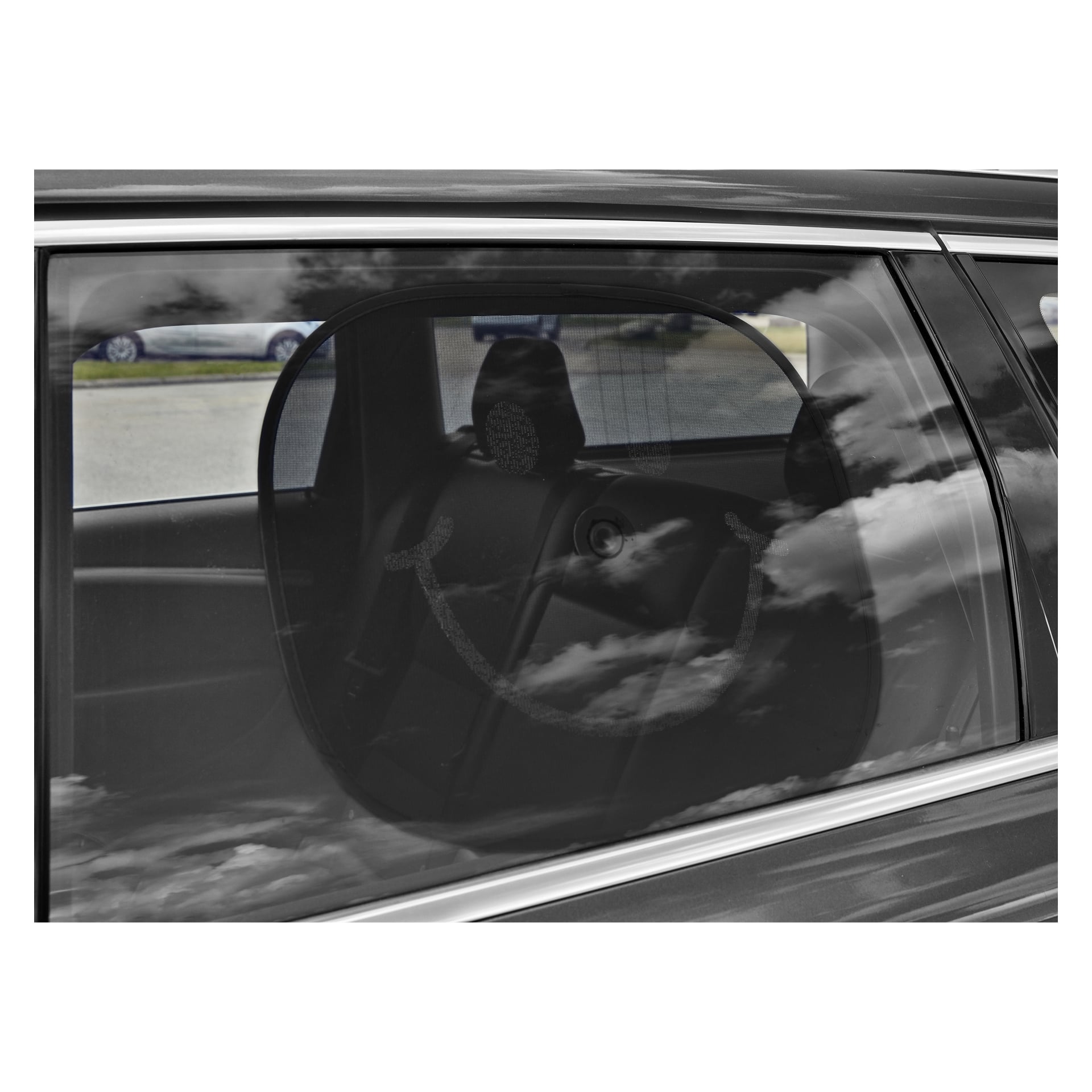 En Hamron Sunshade Smile 2-paknings solskjerm med smilefjes er festet til bilvinduet. Refleksjoner av skyer og et annet kjøretøy vises på glasset, mens bilens interiør og baksete kan sees gjennom den gjennomsiktige solskjermen.