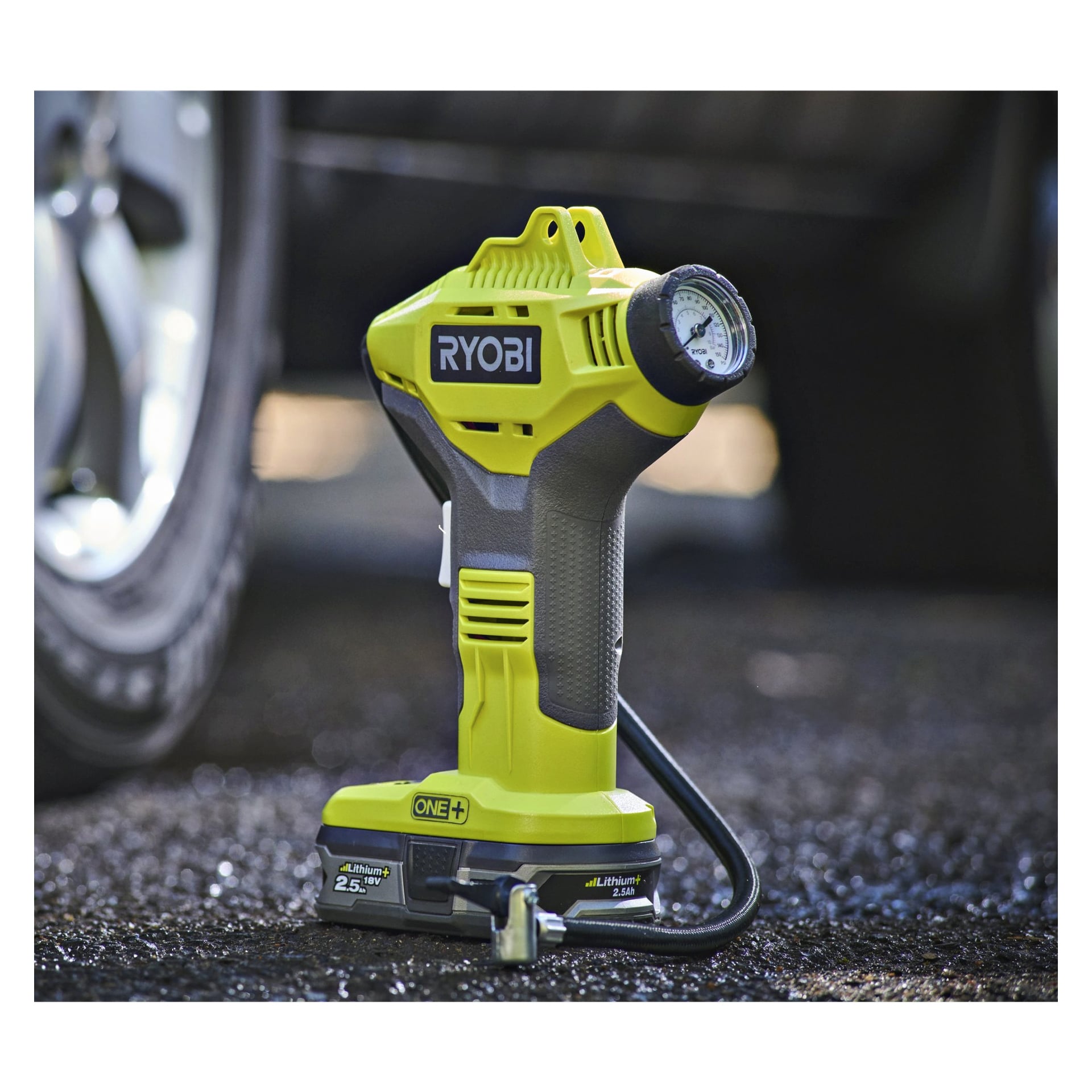 Ryobi One+ Mini-kompressorn R18PI-0 står på asfalt bredvid ett bildäck, förberedd för att pumpas.