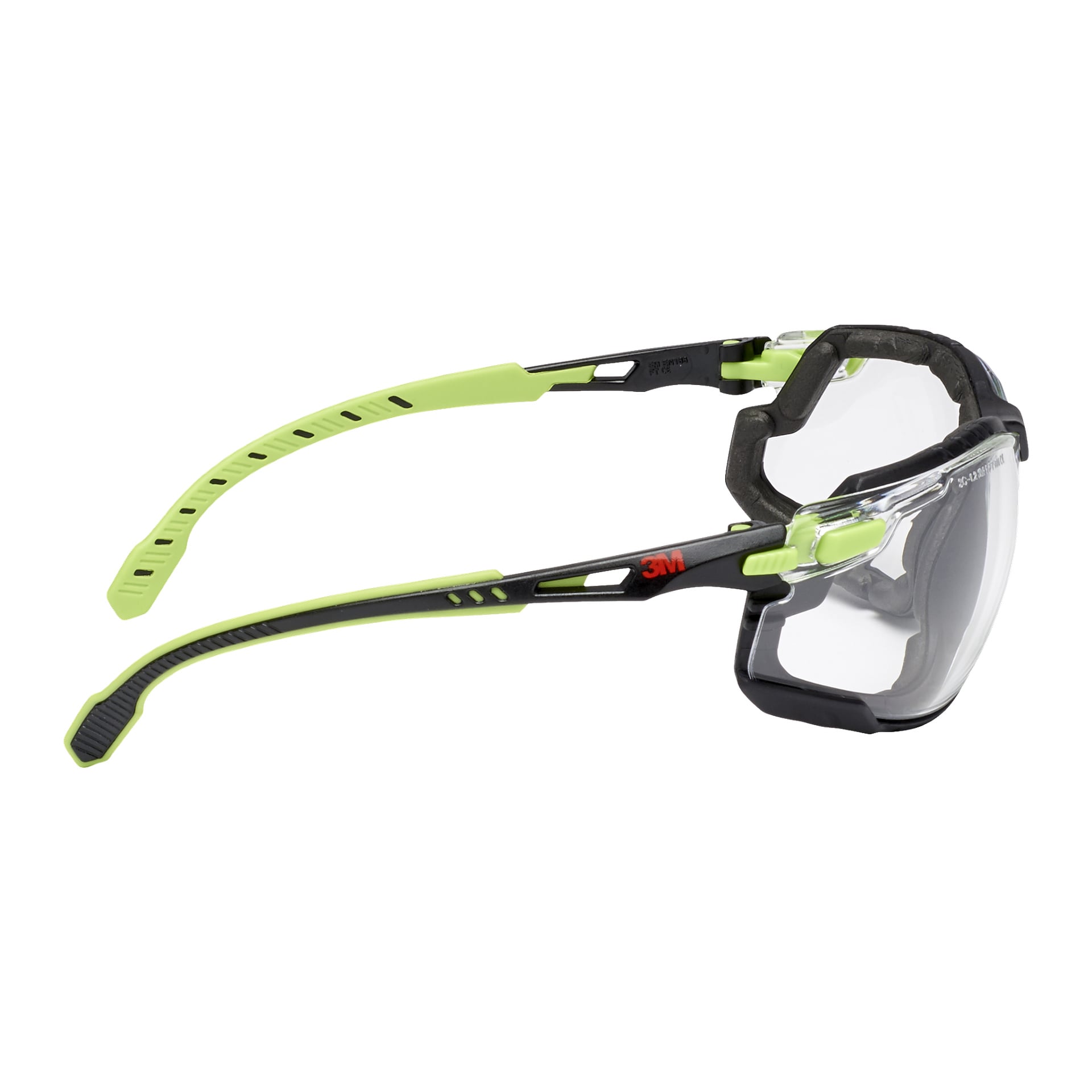 3M Solus Soft 1000 skyddsglasögon har transparenta glas och en skumtätning runt bågarna. Armarna är ergonomiska, färgade i grönt och svart, med justerbar tempeldesign. En röd 3M-logga syns på sidan.