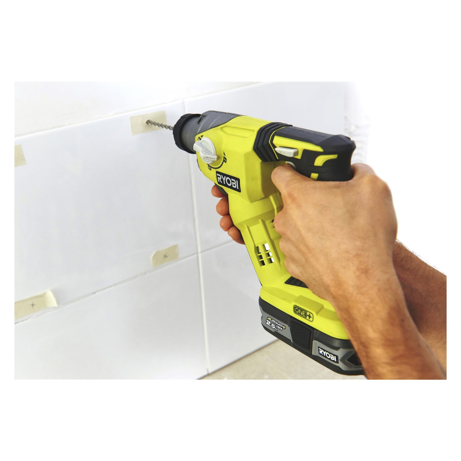 Någon använder en gul och svart Ryobi One+ R18SDS-0 sladdborr för att göra ett hål i en kaklad vit vägg, där flera remsor maskeringstejp fästs på plattorna.