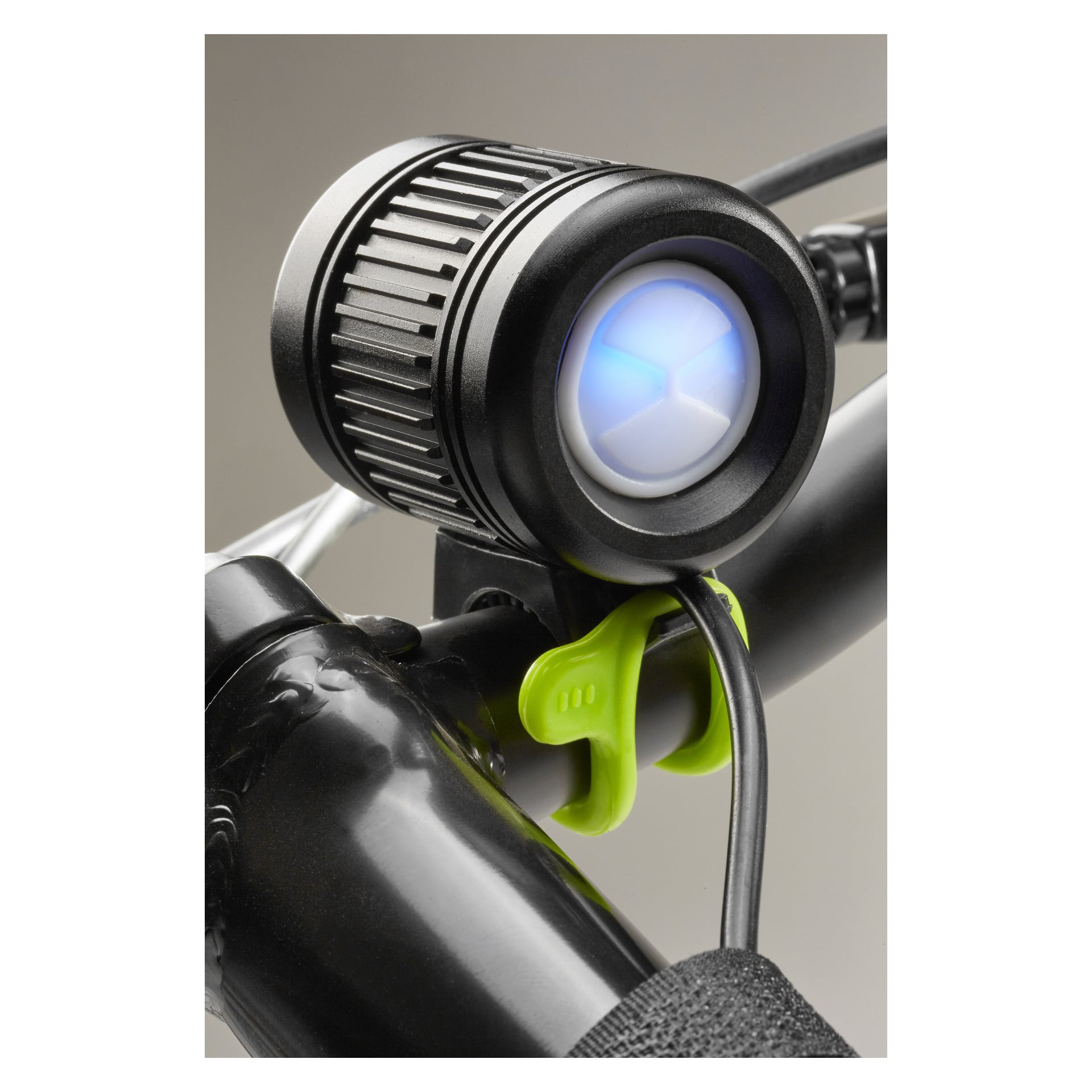 En närbild visar ett svart cykelstyre med en Kayoba Multisport-lampa LED, som lyser med ett blått sken. En grön plastklämma håller lampans strömkabel på plats.