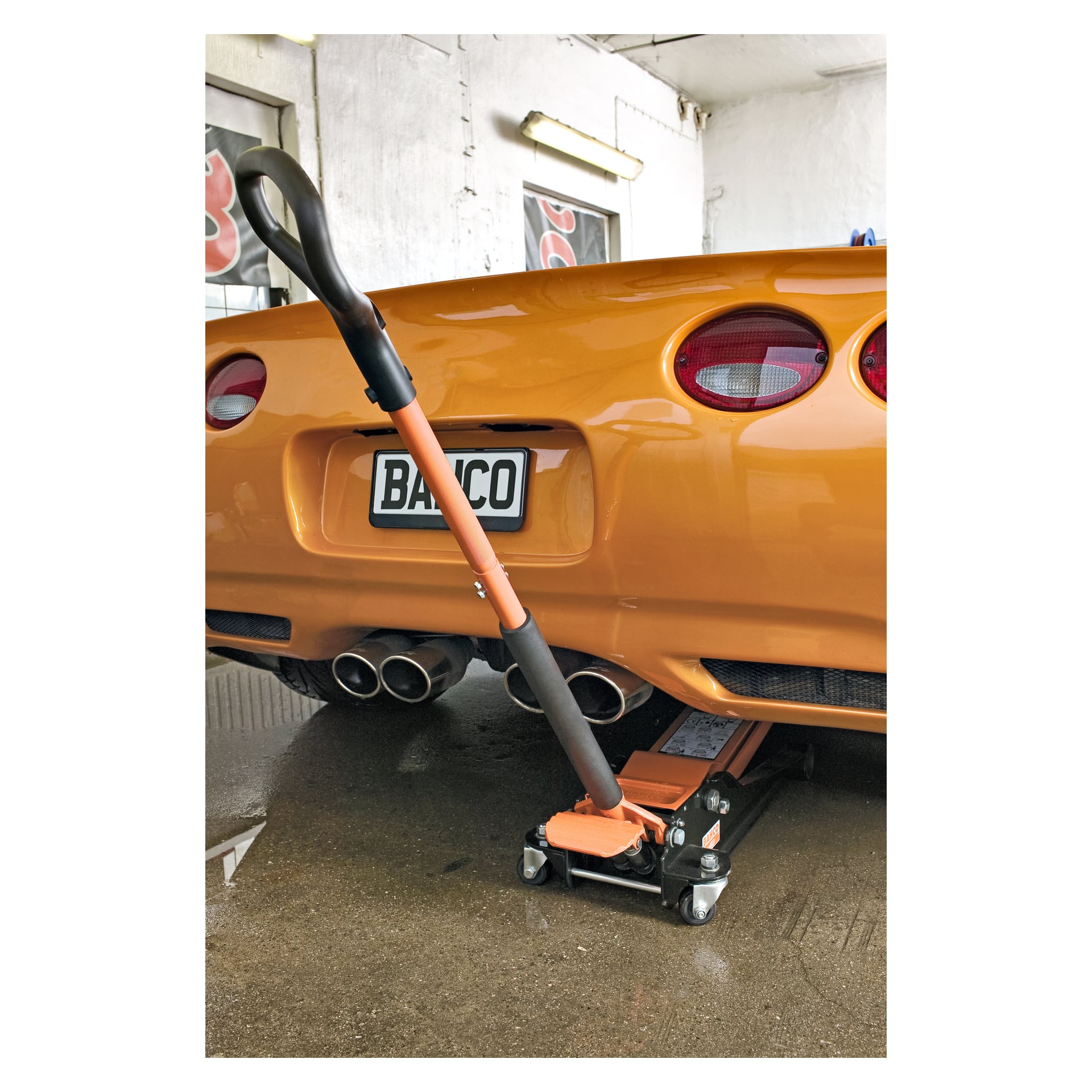 En Bahco BH13000 highlifting-domkraft höjer bakre stötfångaren på en orange sportbil inne i ett garage eller verkstad. Bilen har fyra avgasrör och visar en registreringsskylt märkt BANCO.