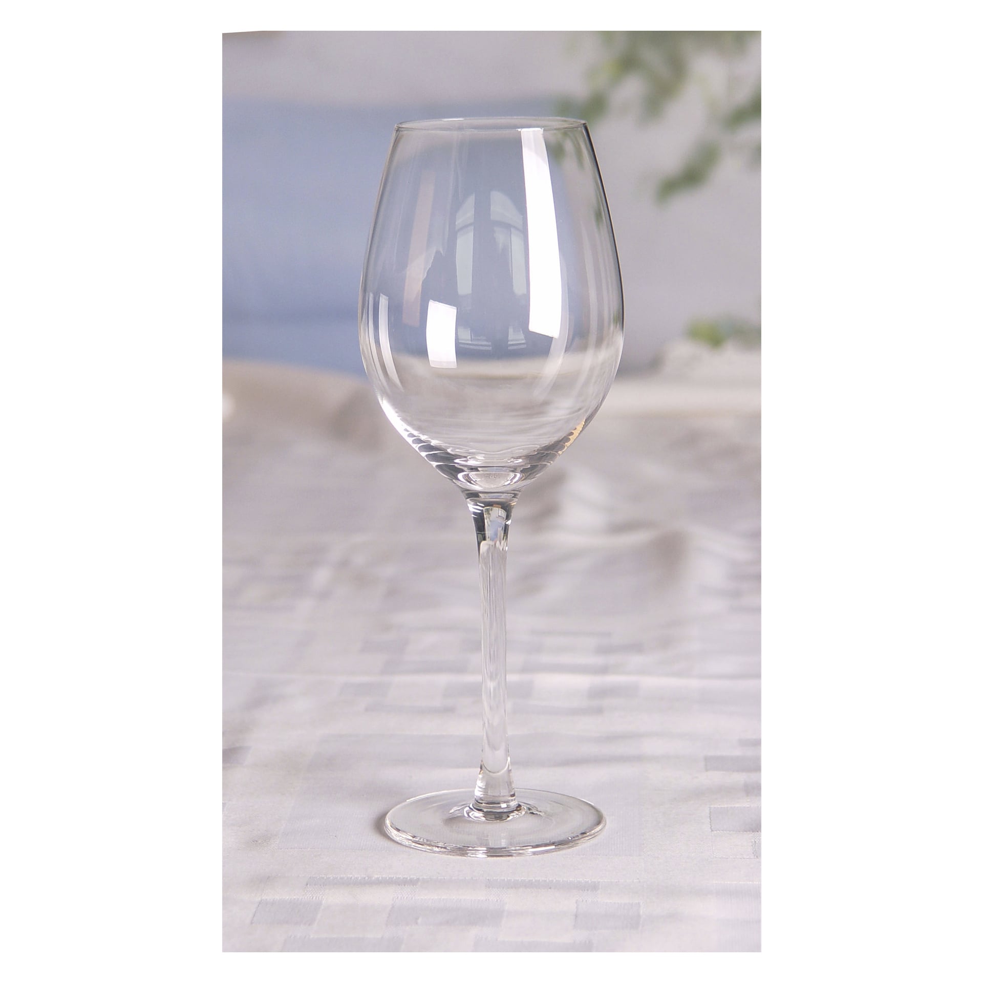 Två genomskinliga Menuett-vinglas från Wine Glasses 2 Pack vilar på en vit bordsduk, med en mjukt suddig bakgrund med subtila färger och inslag av grönska.