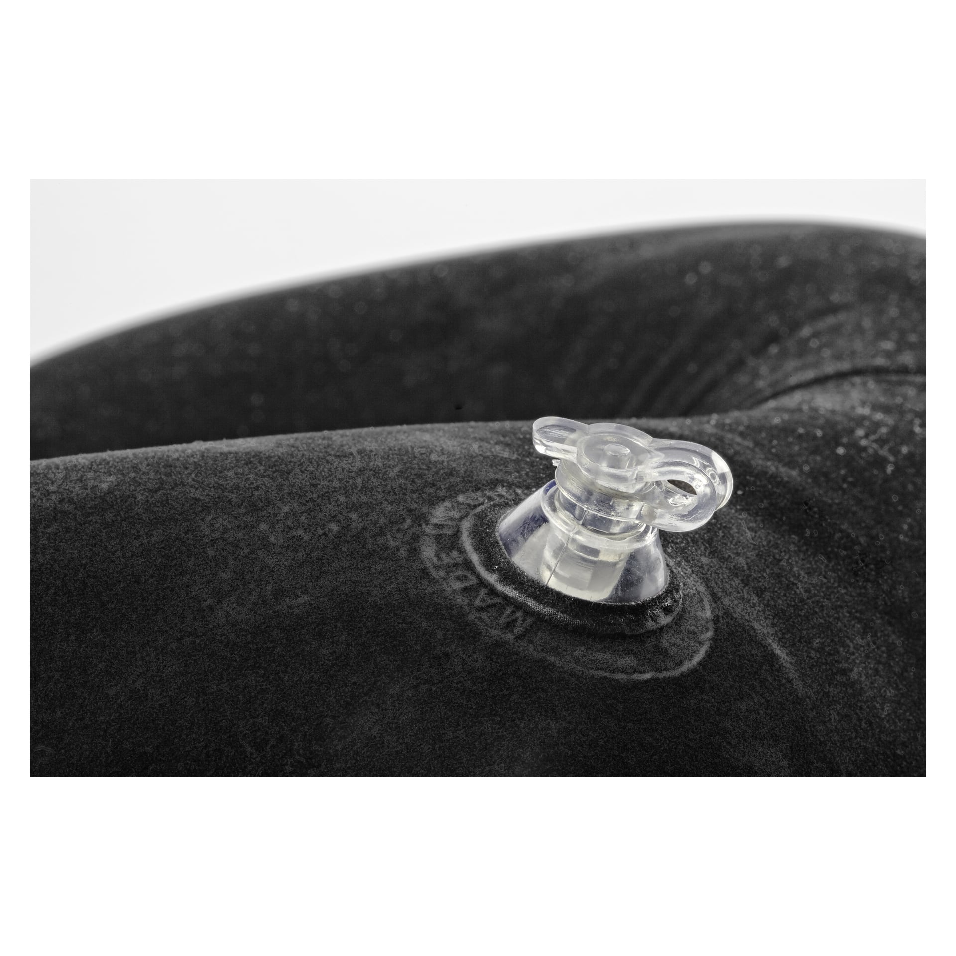 Detaljerad närbild av den genomskinliga plastventilen på Kayoba Travel-kitet, som visar dess uppblåsbara, mjuka och sammetslena mörkgrå yta. Ventilens textur är skarpt fokuserad, med en mjuk suddighet som mjukar upp bakgrundskanterna.