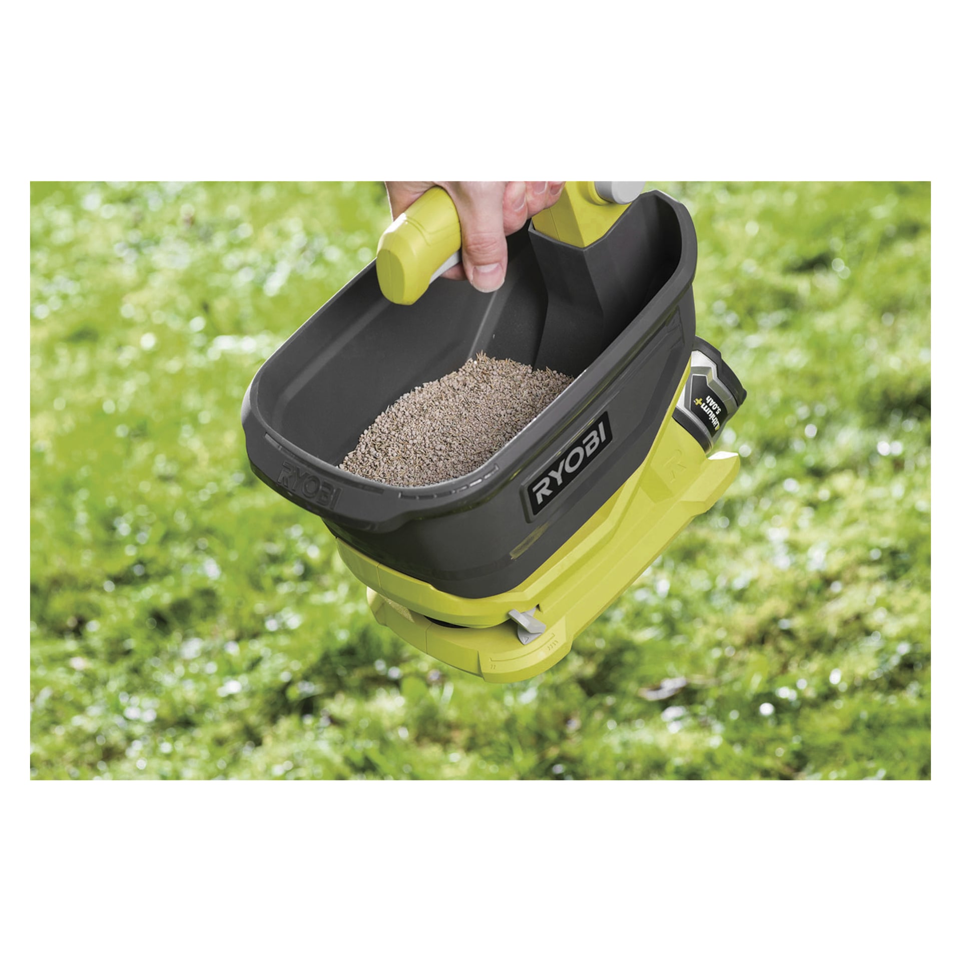 En hand håller en Ryobi One+ OSS1800 batteridriven spridare laddad med granuler, svävande ovanför ett grönt gräsområde.