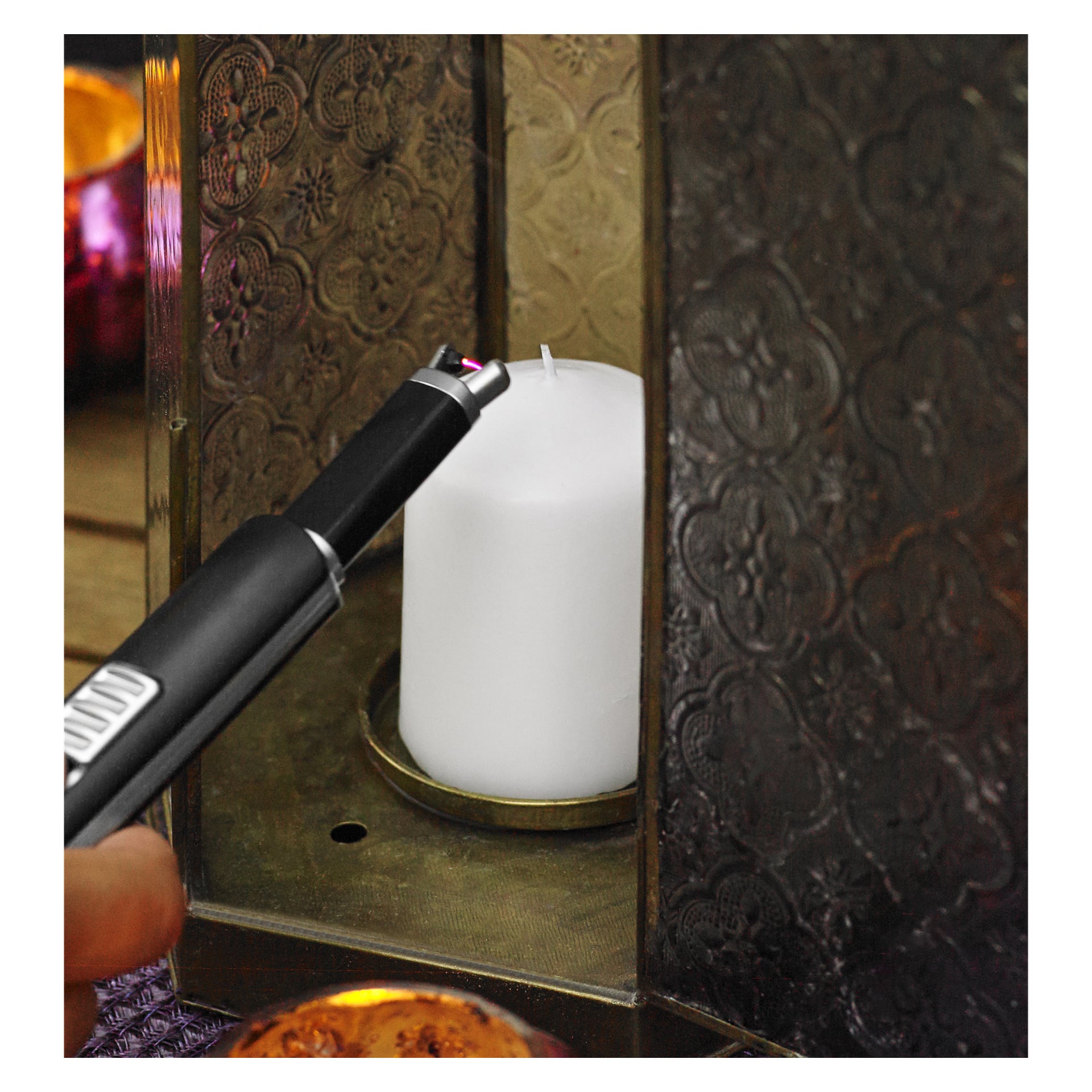 En Menuett USB-lighter holdes nær veken på et hvitt søylelys plassert inne i en utsmykket metalllykt, klar til å tenne lyset.
