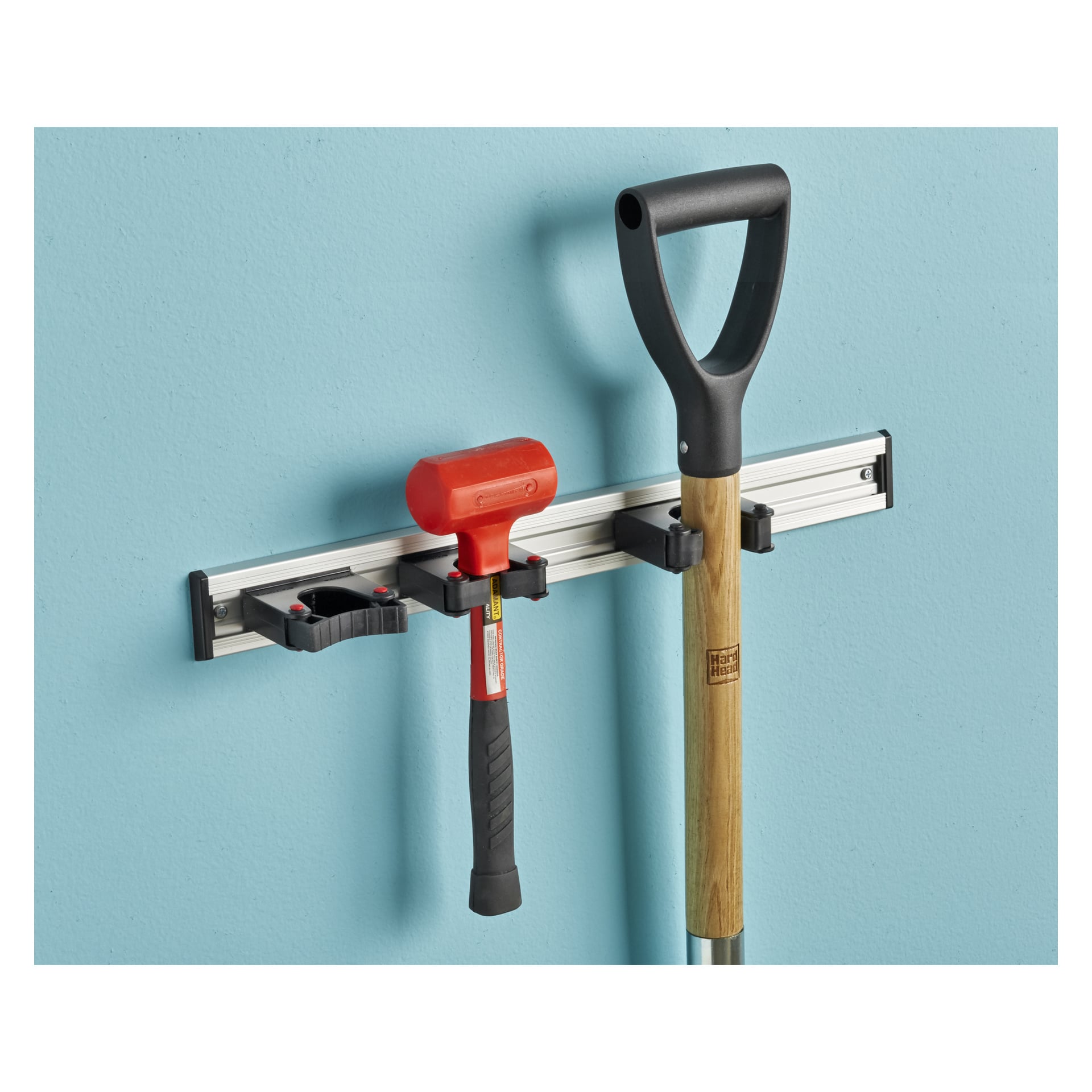 Uchwyt Toolflex Equipment przymocowany do jasnoniebieskiej ściany zabezpiecza czerwony młotek i drewnianą łopatę.