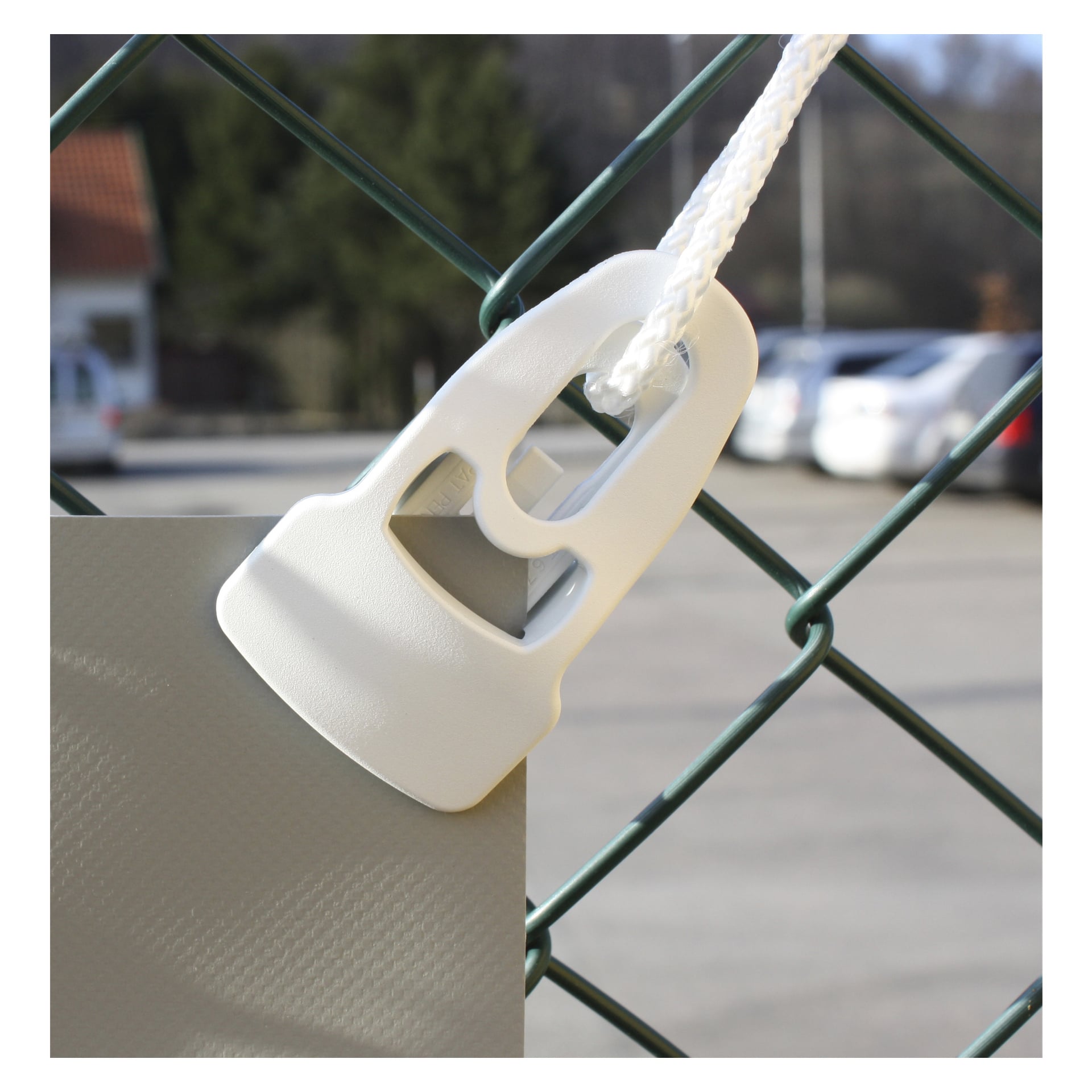En Holdon systems Multi-clamp från fyrpacket är att fästa ett rep och en tygbit i ett grönt trådstängsel, med suddiga parkerade bilar och byggnader i bakgrunden.