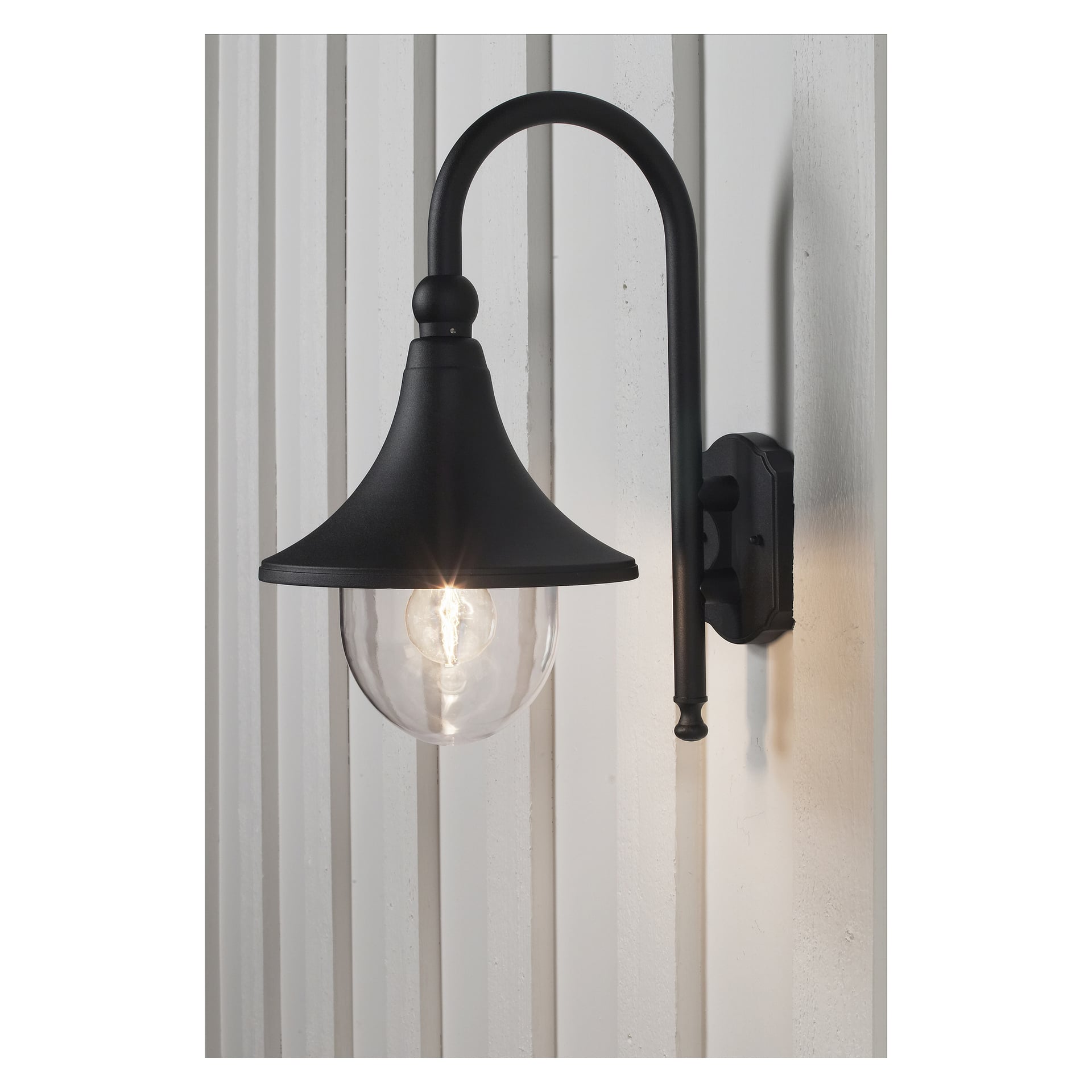 En svart metallvägglampa av Anslut med en böjd arm och en transparent glasglob är fäst vid en vertikal panelvägg. Glödlampan inuti lyser.