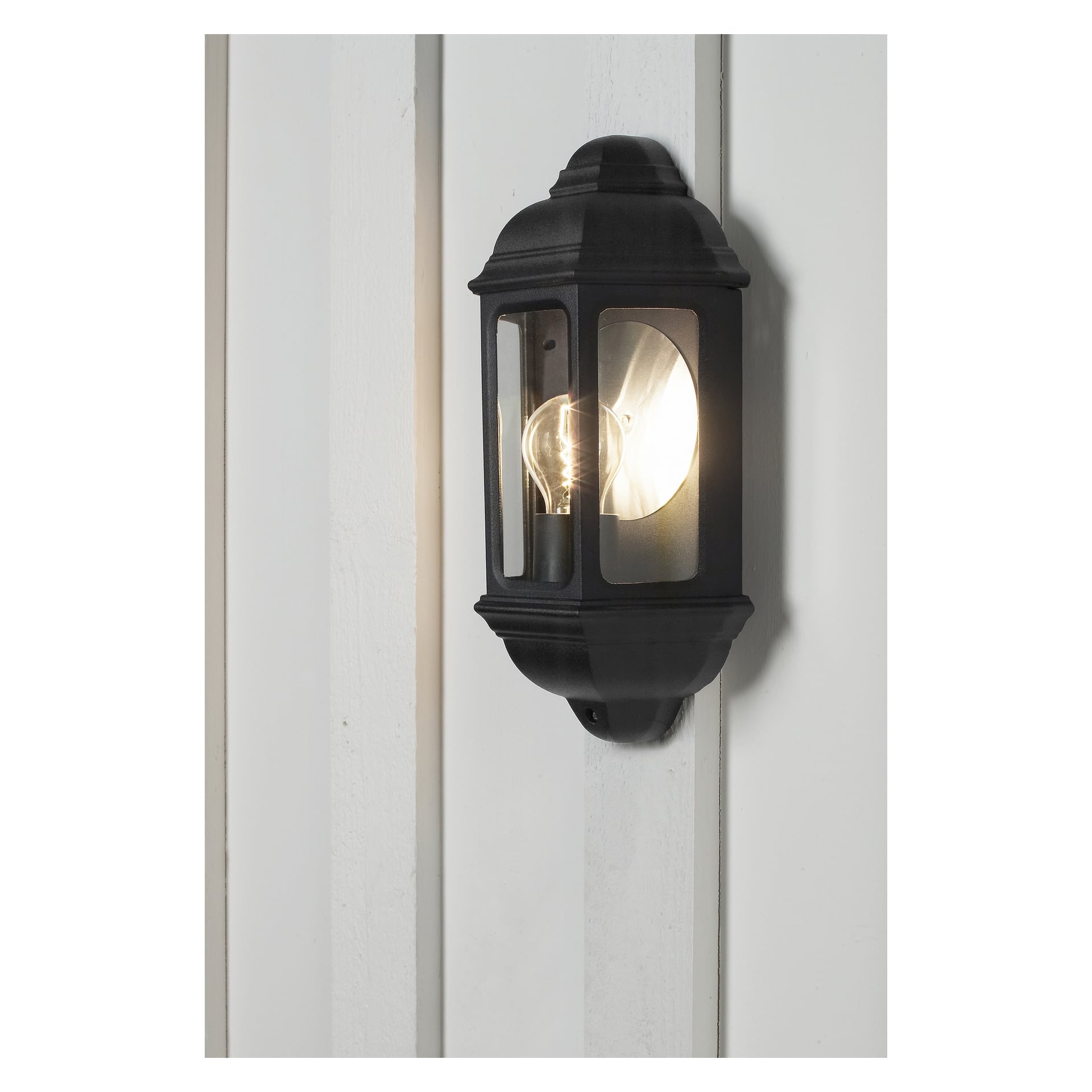 En svart Anslut-vägglampa med klart glasskydd är fäst vid en panelad vägg, dess glödlampa lyser varmt och skapar en inbjudande atmosfär.