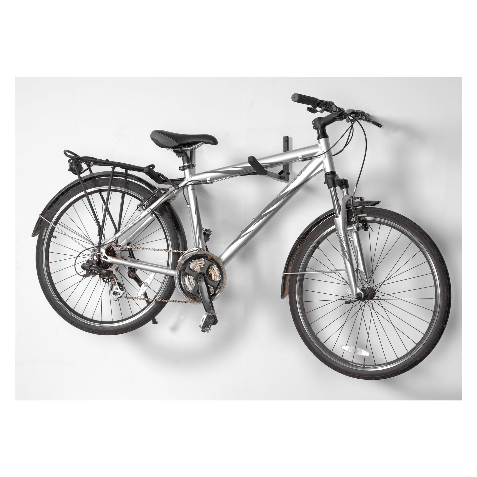 Srebrny rower górski z czarnymi kierownicami i błotnikami jest zamontowany na ścianie wraz z nosidłem Hard Head Bike Carrier. Zawiera tylny bagażnik, zarówno przednie, jak i tylne biegi oraz czarne opony.