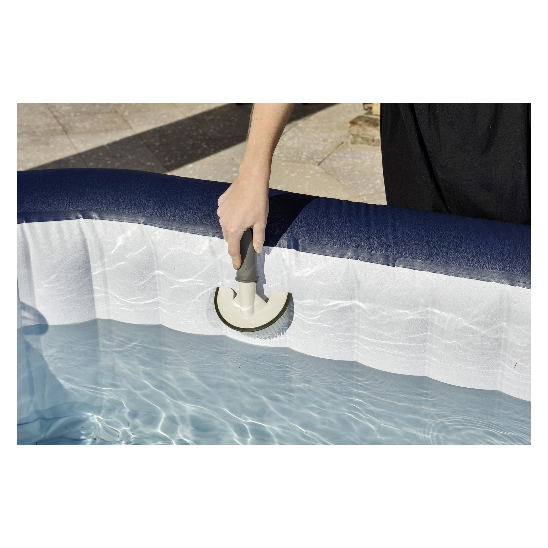 Någon rengör innerväggen på en vattenfylld uppblåsbar pool med det tredelade Bestway Hot Pool cleaning set. Poolen har en mörkblå kant, och personen bär mörka kläder.