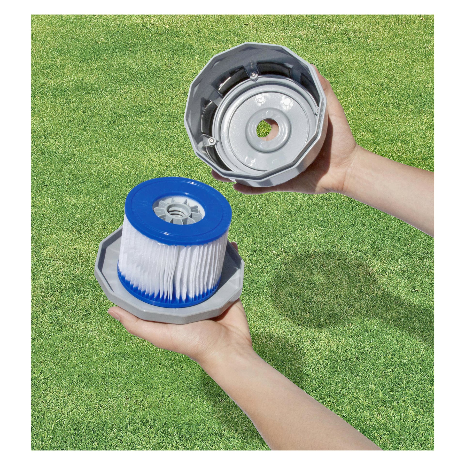Dwie dłonie prezentują elementy filtra Bestway do Spa Bath 2 Pack; Jedną ręką trzyma niebiesko-biały wkład filtra, a druga ma szarą pokrywkę. W tle rozciąga się intensywnie zielony, trawiasty trawnik.