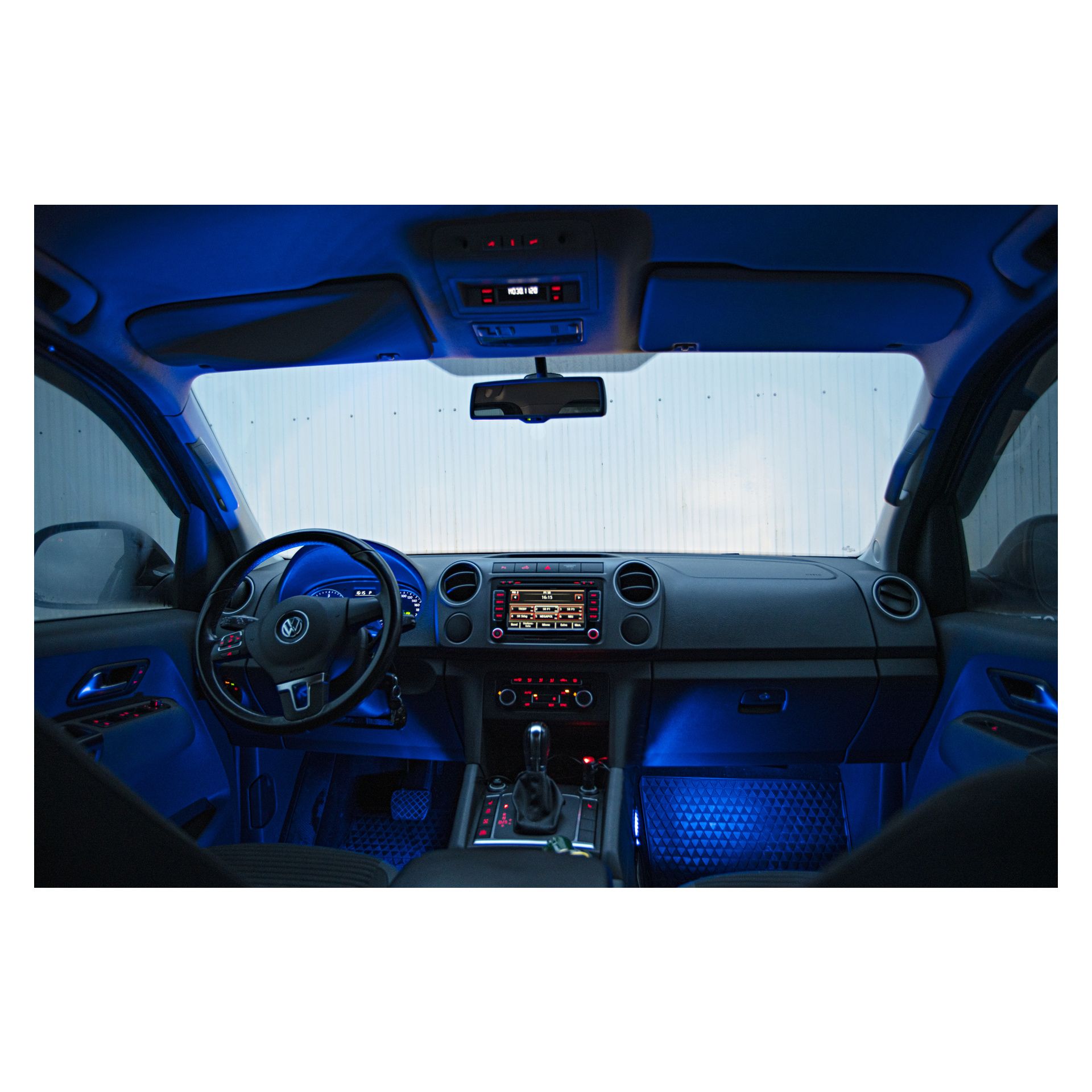 Inuti en Volkswagen badar instrumentpanelen, ratten, mittkonsolen och framsätena i blått sken från Hamron Music Controlled LED Strips 4 Pack. Den parkerade bilen vetter mot en korrugerad metallvägg.