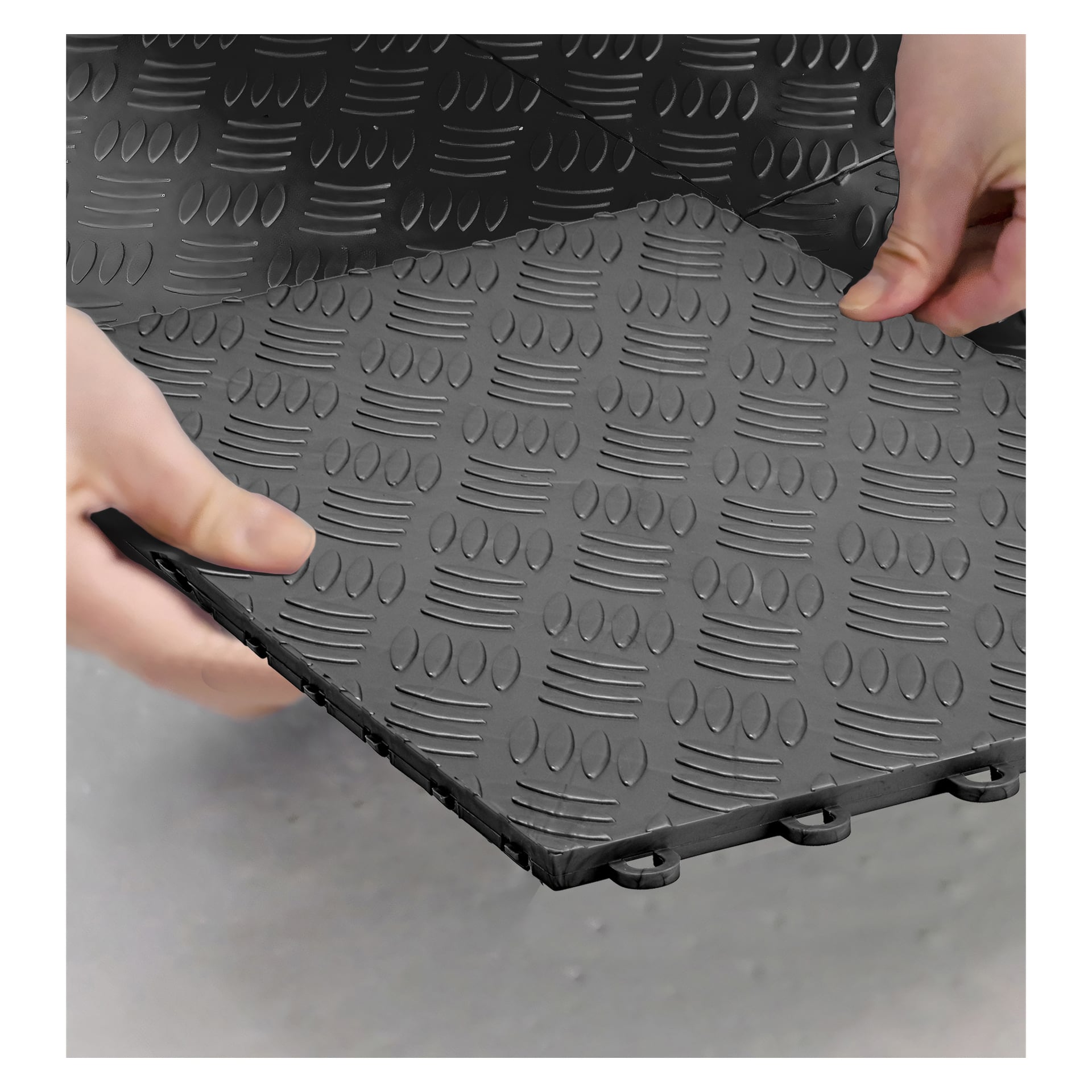 Hendene plasserer en Hard Head Floor-fliser 9-paknings sammenlåst matte med en diamantteksturert overflate på et grått gulv, som viser mattens kantfliker designet for enkel montering.