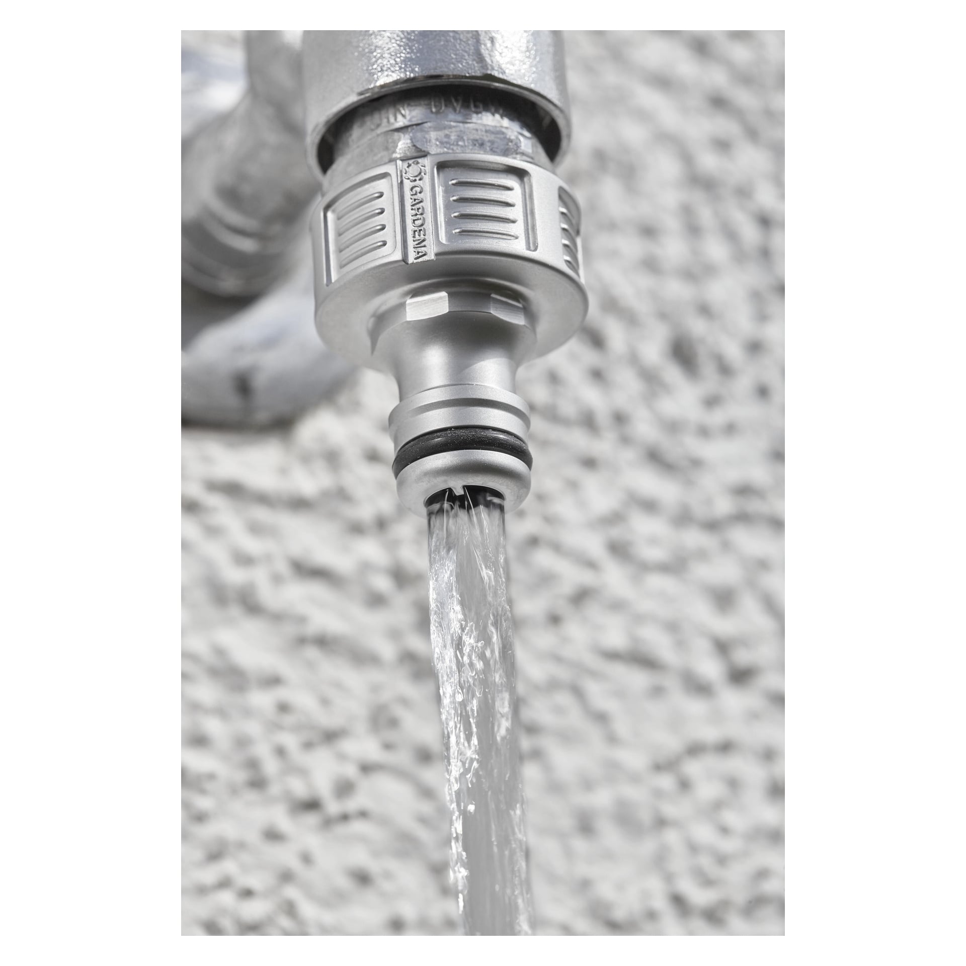 Närbild på en metallkran utomhus med Gardena Tap Connector Premium fäst, vatten strömmar från pipen.