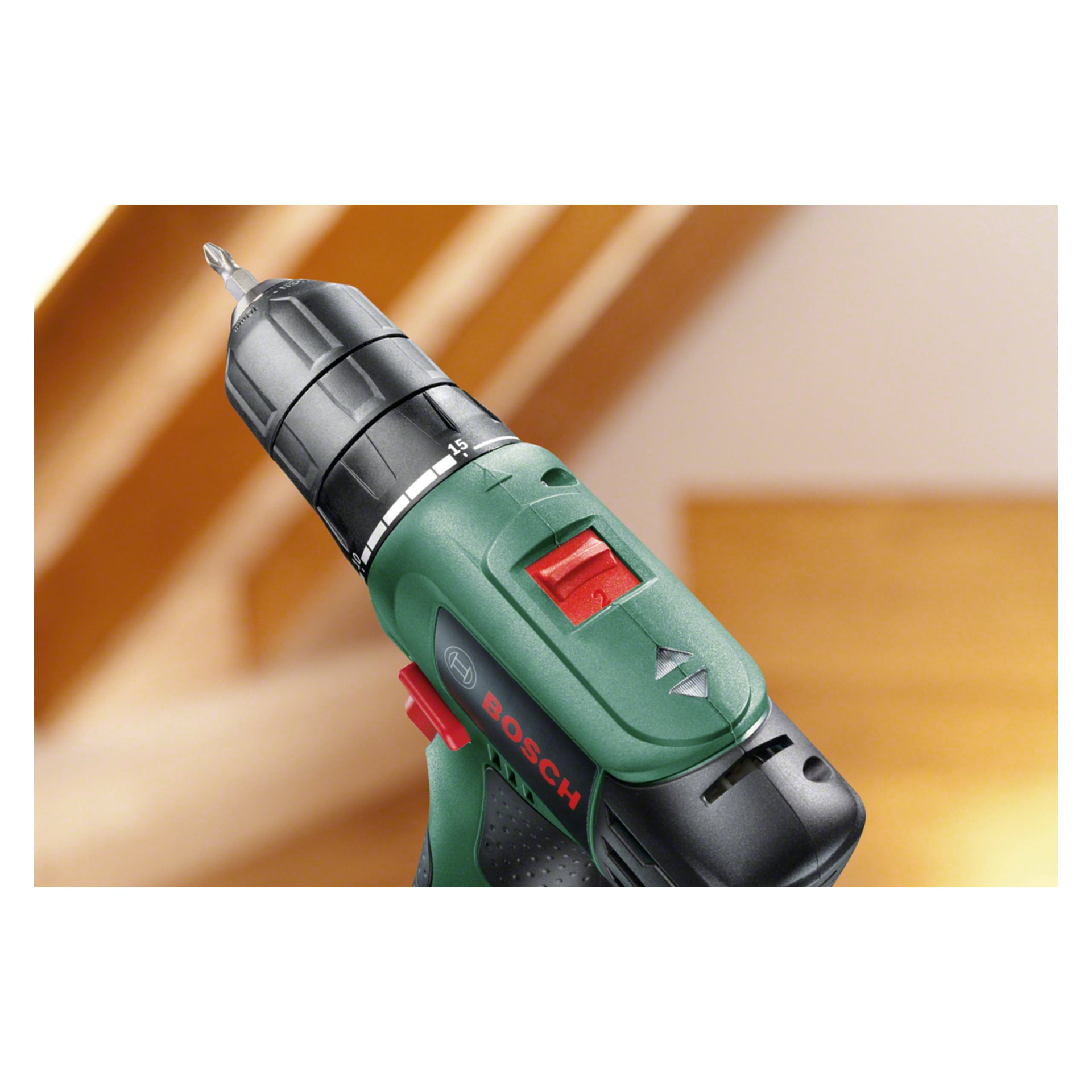 Szczegółowy widok zielonego śrubokręta Bosch Compact wraz z torbą na akcesoria EasyDrill 1200, z czarną uchwytem, czerwonym przełącznikiem i teksturowaną rączką; Scena rozgrywa się wewnątrz, z delikatnie skupionymi drewnianymi schodami za nimi.
