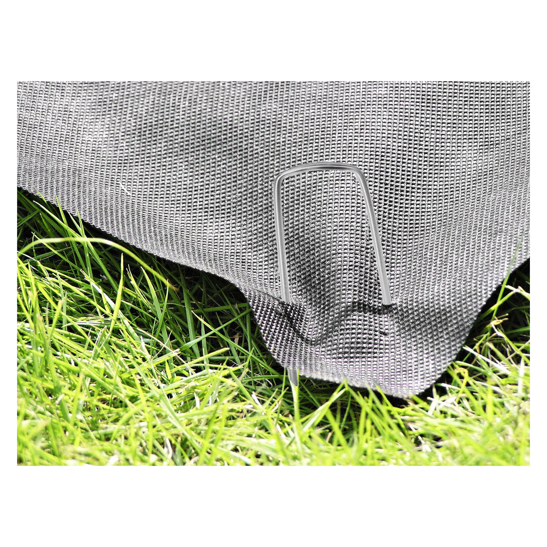 Zbliżenie pokazuje 10-pak metalowych elementów ogrodowych Hard Head Cover Anchor, które przypinają czarną tkaninę ogrodową do ziemi, otoczoną zieloną trawą na krawędziach.
