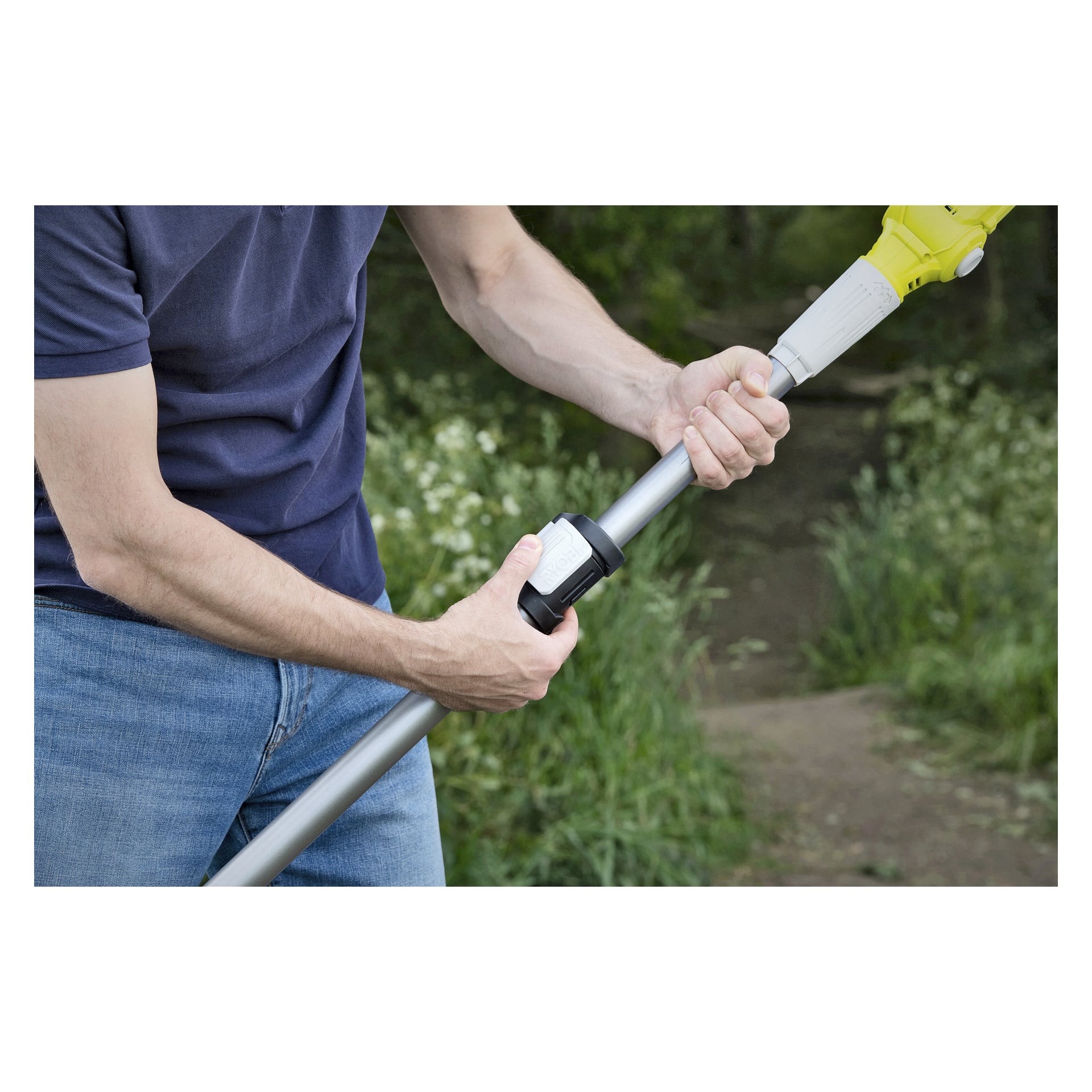 Eine Person in blauer Jeans und marineblauem Hemd steht draußen bei Grün und einem Feldweg und richtet die Metallstange eines Ryobi One+ batteriebetriebenen Langstrecken-Scheren RY18PLA-0.
