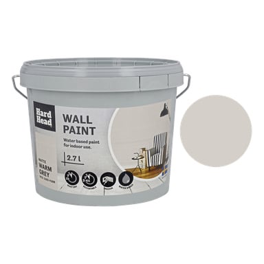 En grå Hard Head Wall Paint-hink i Warm Grey, med en provprov på etiketten tillsammans med ikoner för inomhusanvändning, vattenbaserad sammansättning, matt finish och 2,7-liters volym; förpackningen innehåller också en bild av ett dekorerat rum.