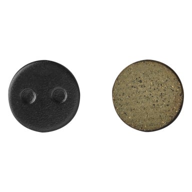 Ett Kayoba Brake Pads 2-pack visas med en svart, rund bromsbelägg med två hål till vänster, och en brunaktig, fläckig, rund bromsbelägg formad som en pressad skiva till höger.