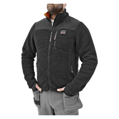 En person står med hendene i lommene, kledd i Bluewear Pro Workwear herrepelsjakke, en svart fleece-glidelås med glidelåslommer, og grå arbeidsbukser med sidelommer.