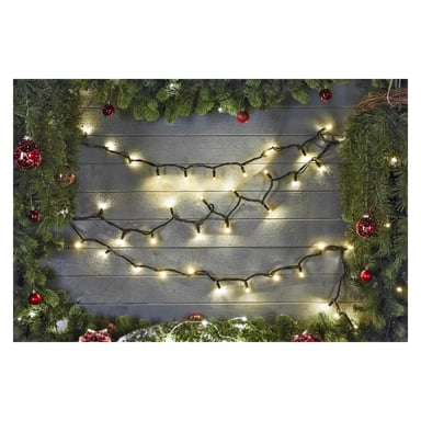 EKVIP LED-ljusslingor från Connectable System hänger längs en grå trävägg, omgiven av gröna tallgirlanger och röda prydnader, vilket ger rummet en glad julkänsla.