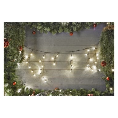 En trävägg kantad med grangrenar är dekorerad med EKVIP:s LED-istappssträng Connectable System och röda ornament. De upplysta ljusen bidrar till en festlig högtidsstämning.