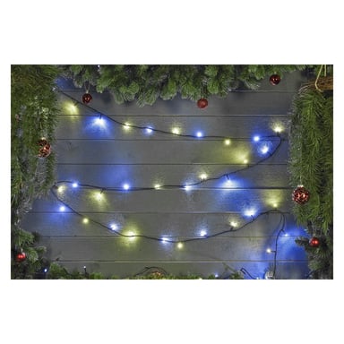 Grön girland och röda prydnader hänger över en trävägg, accentuerade av EKVIP LED-ljusslingor i blått och vitt som zickzackar mjukt över ytan. Frodig grönska ramar in toppen och sidorna av displayen.