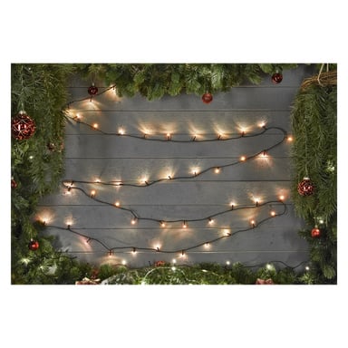 Ständigt gröna girlanger, röda prydnader och EKVIP String Light är placerade längs en trävägg och bildar en festlig kant med ett tomt utrymme i mitten omgivet av dekorationerna.