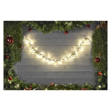 EKVIP LED-lyslenker arrangert i en buet, smilelignende form på en grå trevegg, kantet med furugrener og røde julepynt for et festlig uttrykk.
