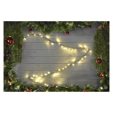 Gröna tallgrenar och röda ornament ramar in en grå trävägg, med EKVIP LED-ljusslingor hängande i ett löst zickzackmönster längs mitten.
