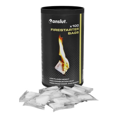 En svart cylindrisk behållare märkt "Anslut Firestarter bags 100 pack" står upprätt och visar en flamgrafik och produktinformation på etiketten, med flera individuellt inslagna vita firestarter-påsar placerade framför.
