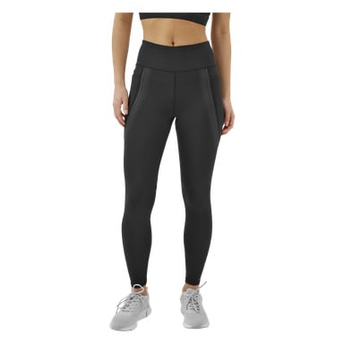 En person visas från mitten av bålen till fötterna, vänd framåt och klädd i en svart sport-bh, högmidjade svarta Kayoba Tights damleggings i Boston med sidosömmar och vita sportsneakers.