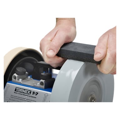 Noen holder en Tormek SP-650 rektangulær slipestein med begge hender, og presser den mot den roterende slipeskiven på en Tormek vannkjølt slipemaskin.