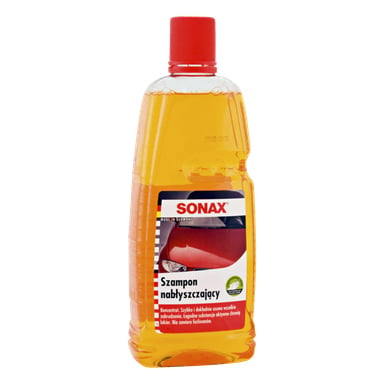 Butelka szamponu Sonax Gloss z czerwonym nakrętką i wypełniona pomarańczowym płynem. Na etykiecie widnieje czerwony samochód oraz napis opisujący jego zalety czyszczące i polerujące.