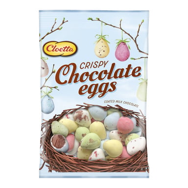 Ett paket med "Cloetta Crispy Chocolate Eggs" innehåller pastellfärgade, fläckiga chokladägg samlade i kluster, med fler ägg hängande från grenarna ovanför. Etiketten anger att detta är mjölkchokladägg med ett överdrag.